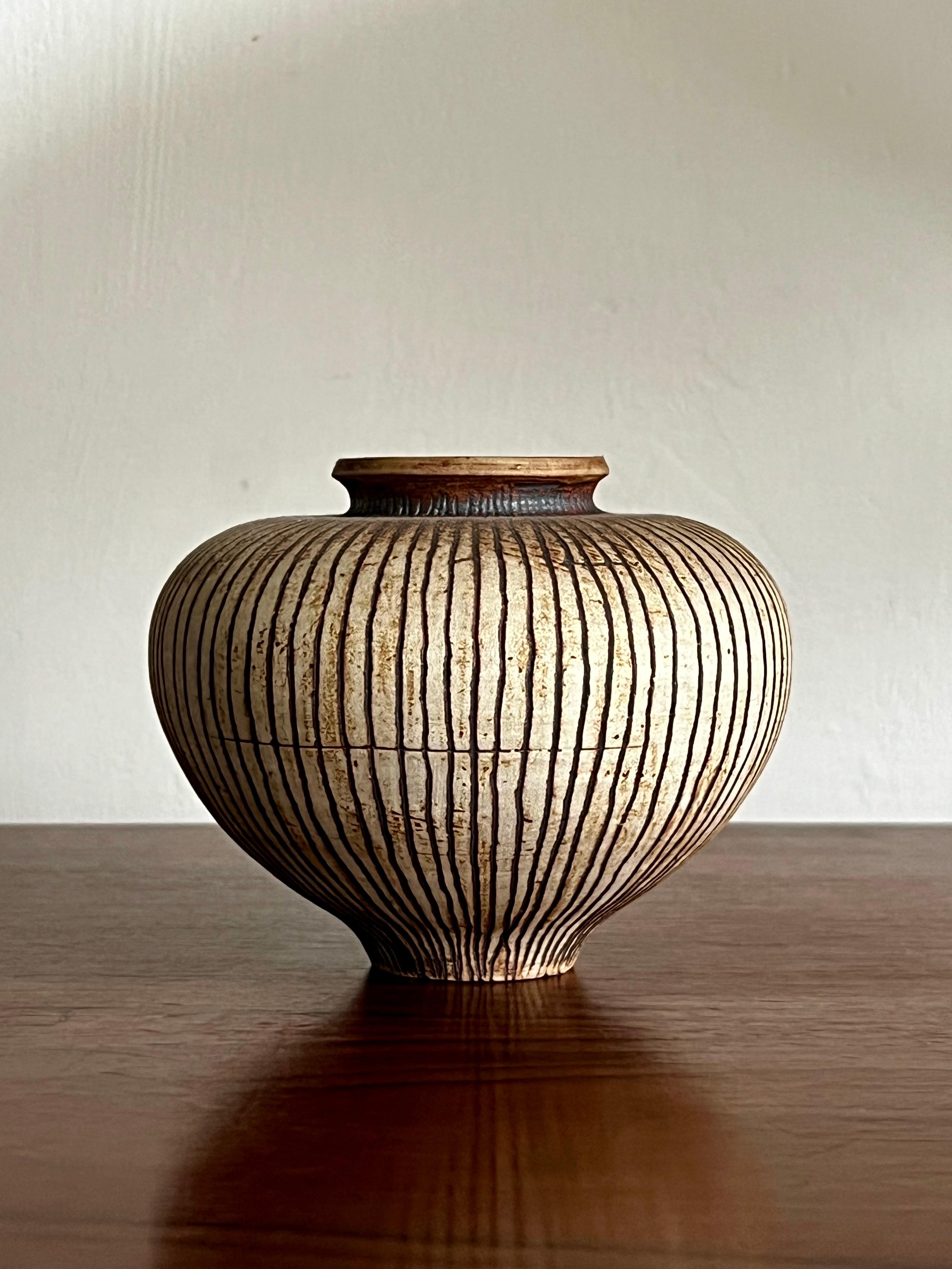 A small ceramic vessel by renowned British potter Waistel Cooper (1913-2009).

The organic shape is decorated with handmade vertical - and occasional lateral - sgraffito lines - in natural tones of cream and brown, best shown in the main image.