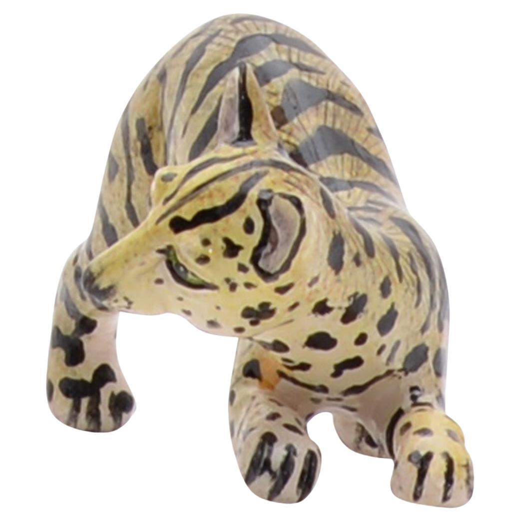 Cette petite sculpture d'un chat serval africain capture l'élégance tranquille et la nature insaisissable du félin. Perché sur un rondin sculpté, le serval est sculpté et peint à la main avec un réalisme et un soin remarquables. Ses grandes oreilles
