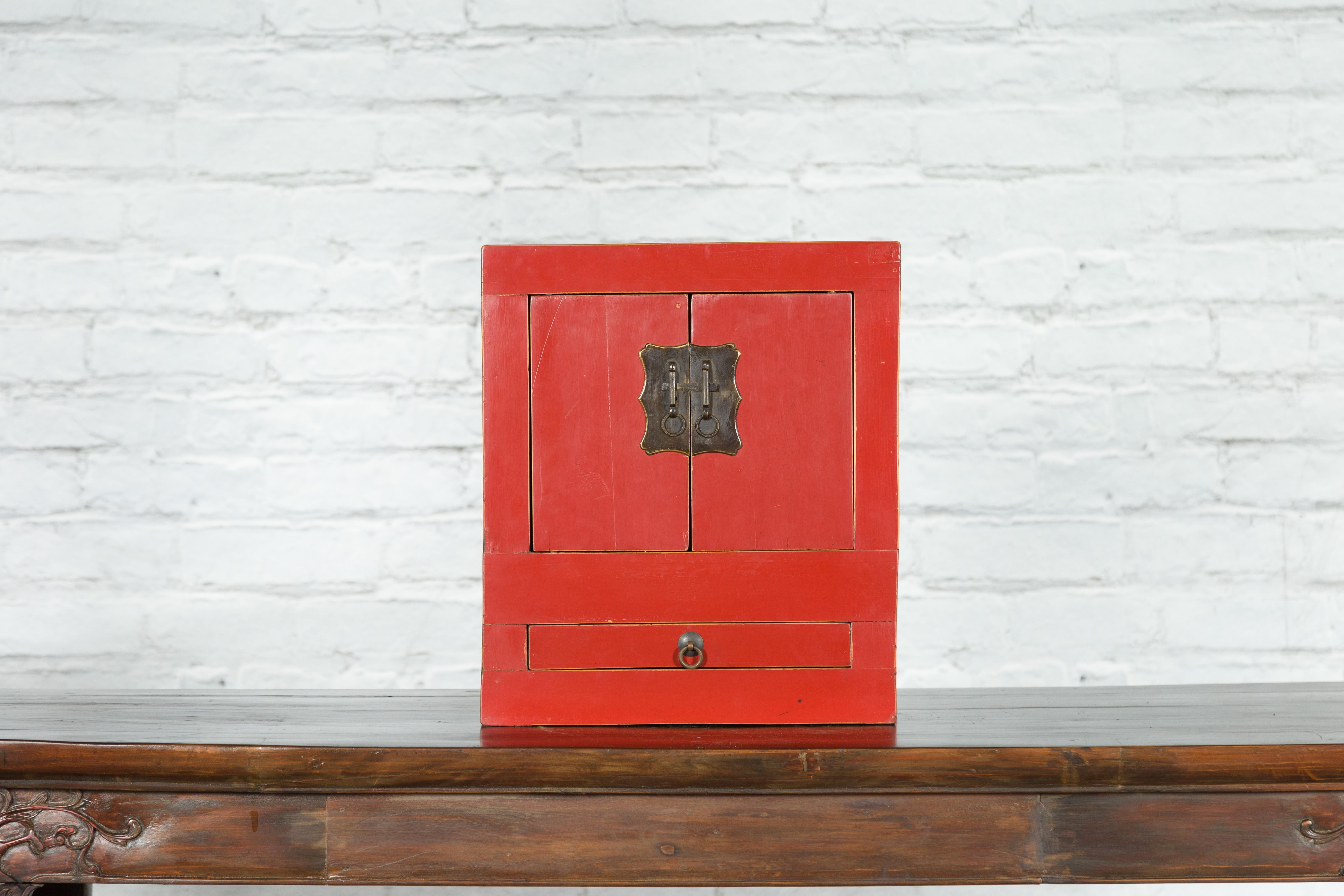A small Chinese red lacquer cabinet from the early 20th century, with brass hardware and lower drawer. Created in China, this cabinet is characteristic of the early 20th century Chinese style. Showcasing a linear silhouette, the cabinet features two