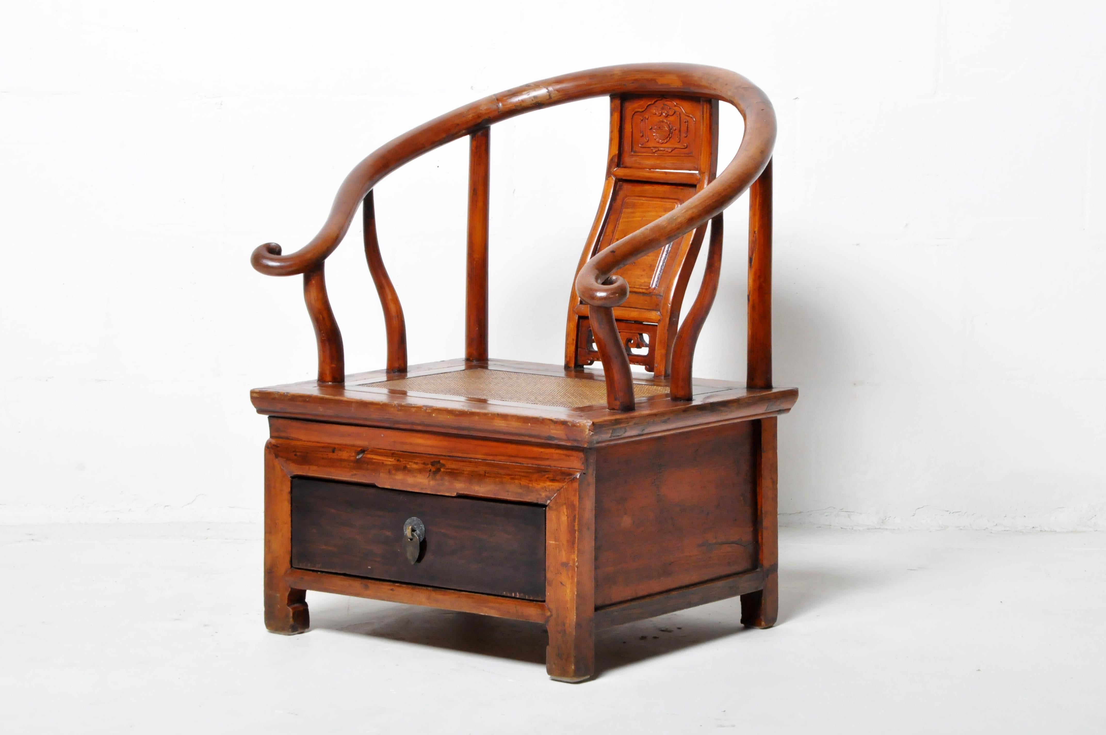 This antique low Chinese chair features an elmwood construction with a curved back. The seat has a drawer for extra storage. The elm is finished with a clear lacquer that shows the grain of the wood. Wear consistent with age and use.
 