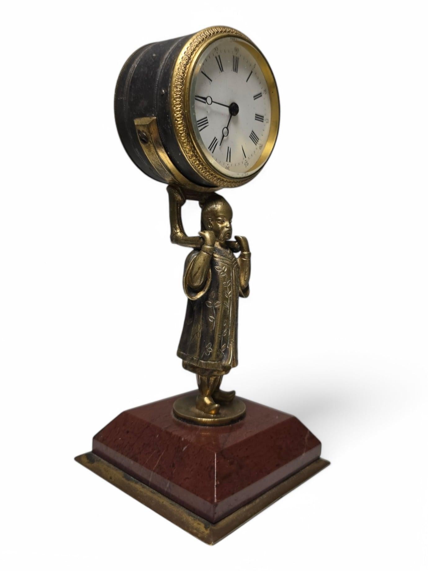 Interesting Chinese clock made of bronze, depicting a delicately sculpted Asian figure holding the clock face. The piece sits on an elegant red marble base, providing an attractive visual contrast and a touch of sophistication. This clock, with