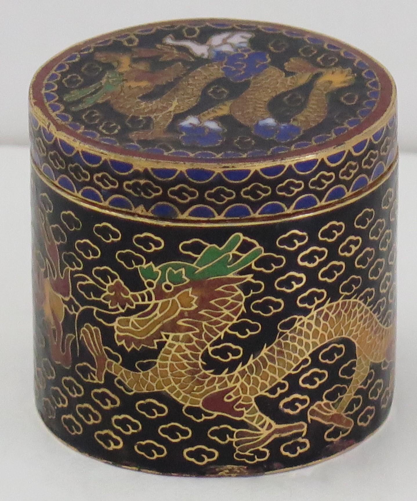 This is a very decorative Chinese cloisonné lidded box which we date to the mid 20th century.

The box has a cylindrical shape, with its original lid and is all beautifully made with colored enamels set into a black ground. 

The main decoration