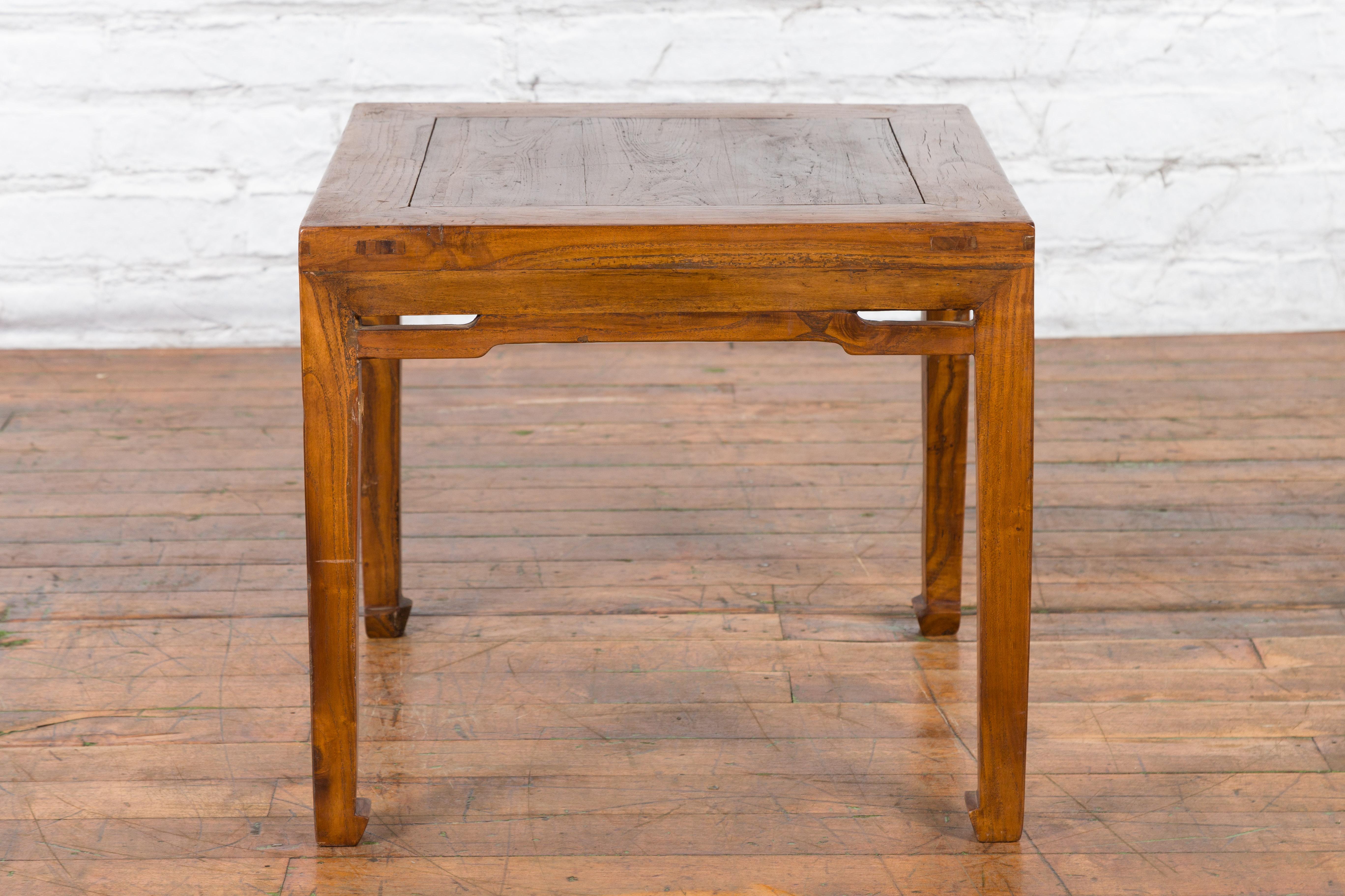 Table basse chinoise ancienne du début du XXe siècle avec des traverses en dos d'âne et des extrémités en sabot de cheval. Créée en Chine au début du XXe siècle, cette petite table basse présente un plateau carré avec une planche centrale, reposant