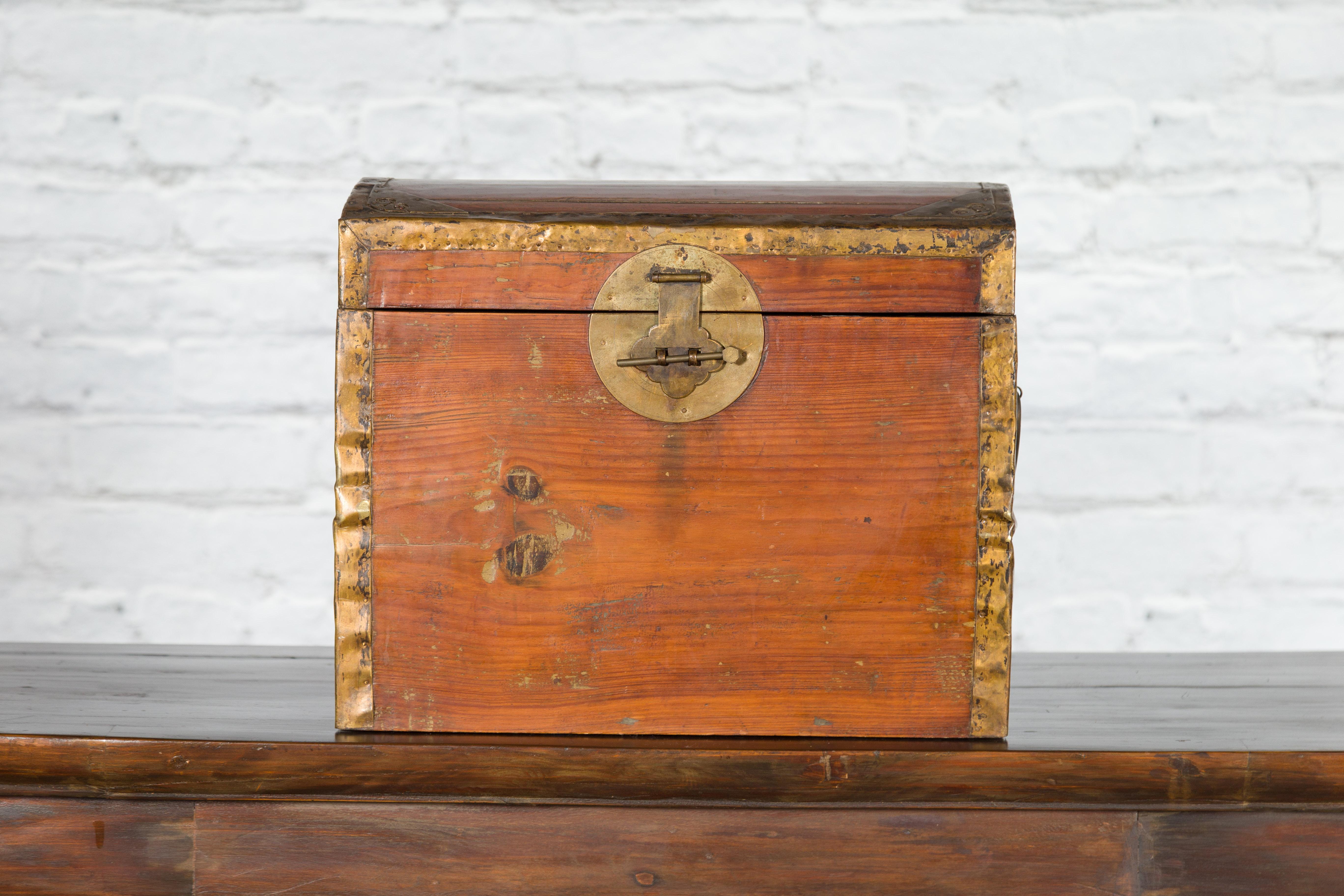 A small Chinese wooden trunk from the early 20th century, with domed lid, brass accents and weathered appearance. Created in China during the early years of the 20th century, this small wooden trunk captures our attention with its simple lines and