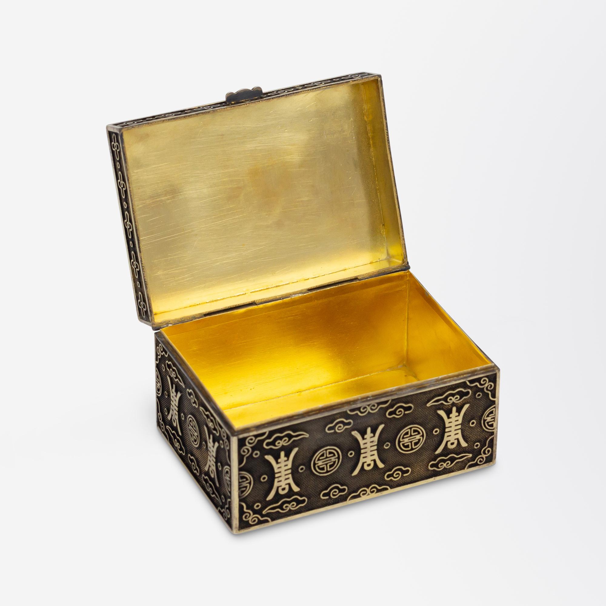 This small silver box was crafted in China and has been inset with a carved jade plaque to the lid. The rectangular box is simply marked 'silver' and is decorated to the exterior with auspicious symbols and cloud motifs which are in relief allowing