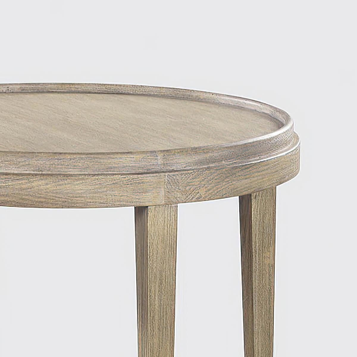 Une table d'appoint ronde de style classique avec une finition peinte grise rustique et légèrement vieillie montrant de légers accents de grain dans le placage celtique. Cette table d'appoint à deux niveaux présente un plateau en bois à galons, des