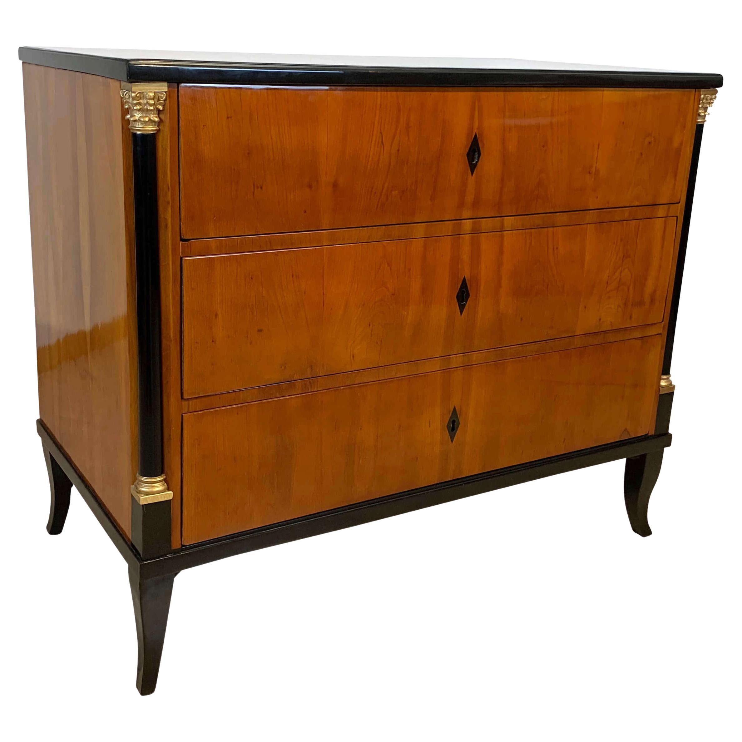 Rare small neoclassical early Biedermeier Commode or Chest of Drawers from South Germany around 1820.
Veneered in wonderful bright cherry wood on spruce softwood. Ebonized legs and cornice. Inlaid and ebonized key coats of arms. Ebonized Half