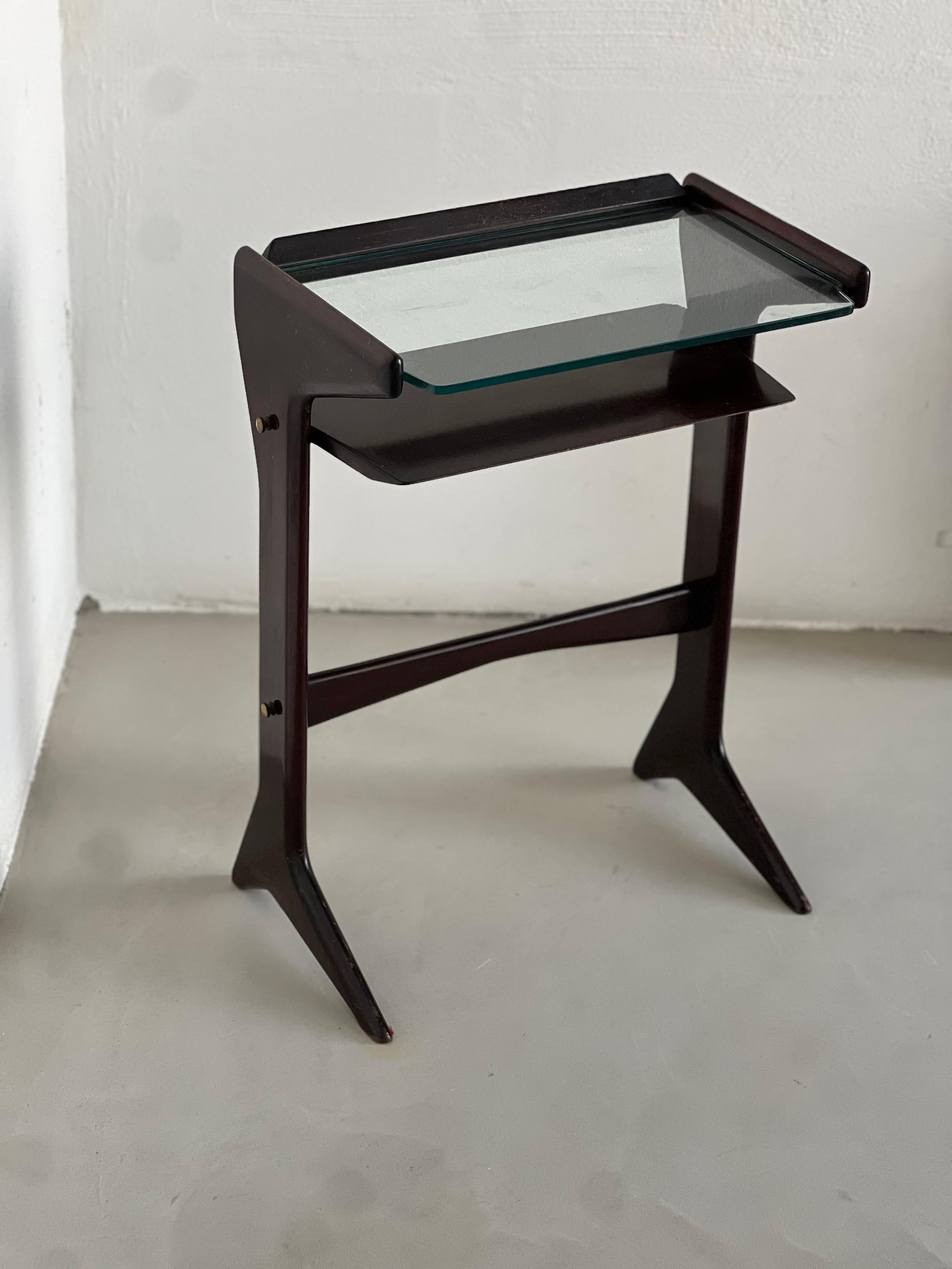 Small and compact console or entrance table with a notable shape made by the carved wood legs that hold a wood shelve and a smaller glass shelve above .

Designed by Ico Parisi and produced in Cantù near Lake Como by De Baggis cabinet maker,
This is