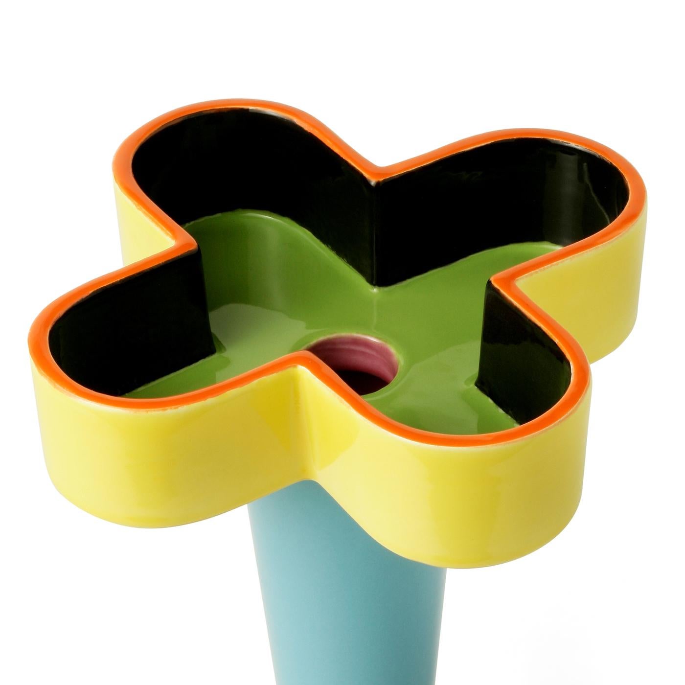 Questo sorprendente vaso multicolore in argilla bianca presenta una bocca a forma di croce. L'esterno della croce è rifinito in giallo vivo con un bordo superiore arancione, mentre l'interno è in verde con un fondo scuro. Questo pezzo è stato