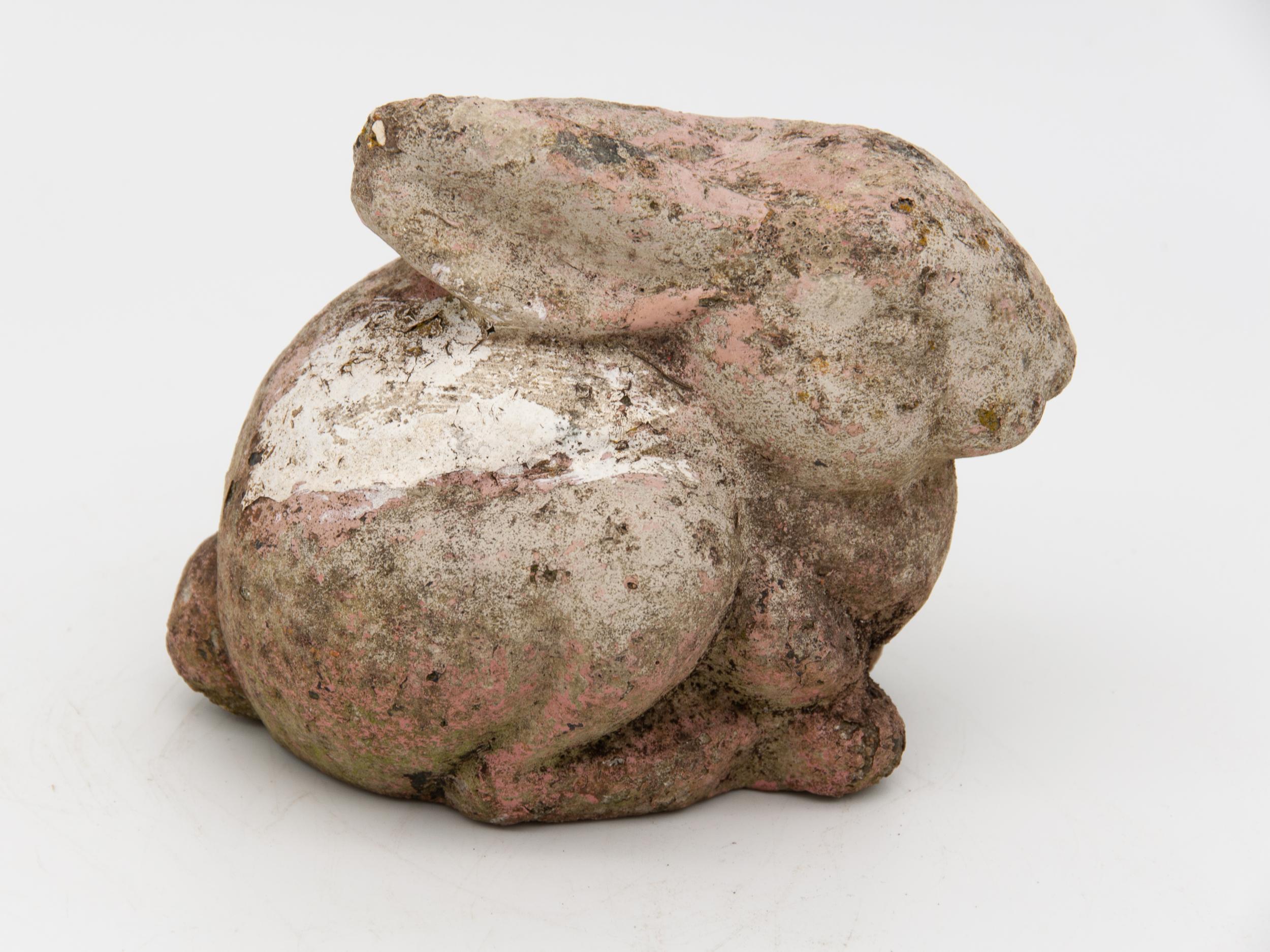 A small stone rabbit or bunny garden ornament with remnants of pale pink paint and a beautiful natural outdoor patina and age. Made from cast stone in the UK, Early 20th century. Wear consistent with age and use.