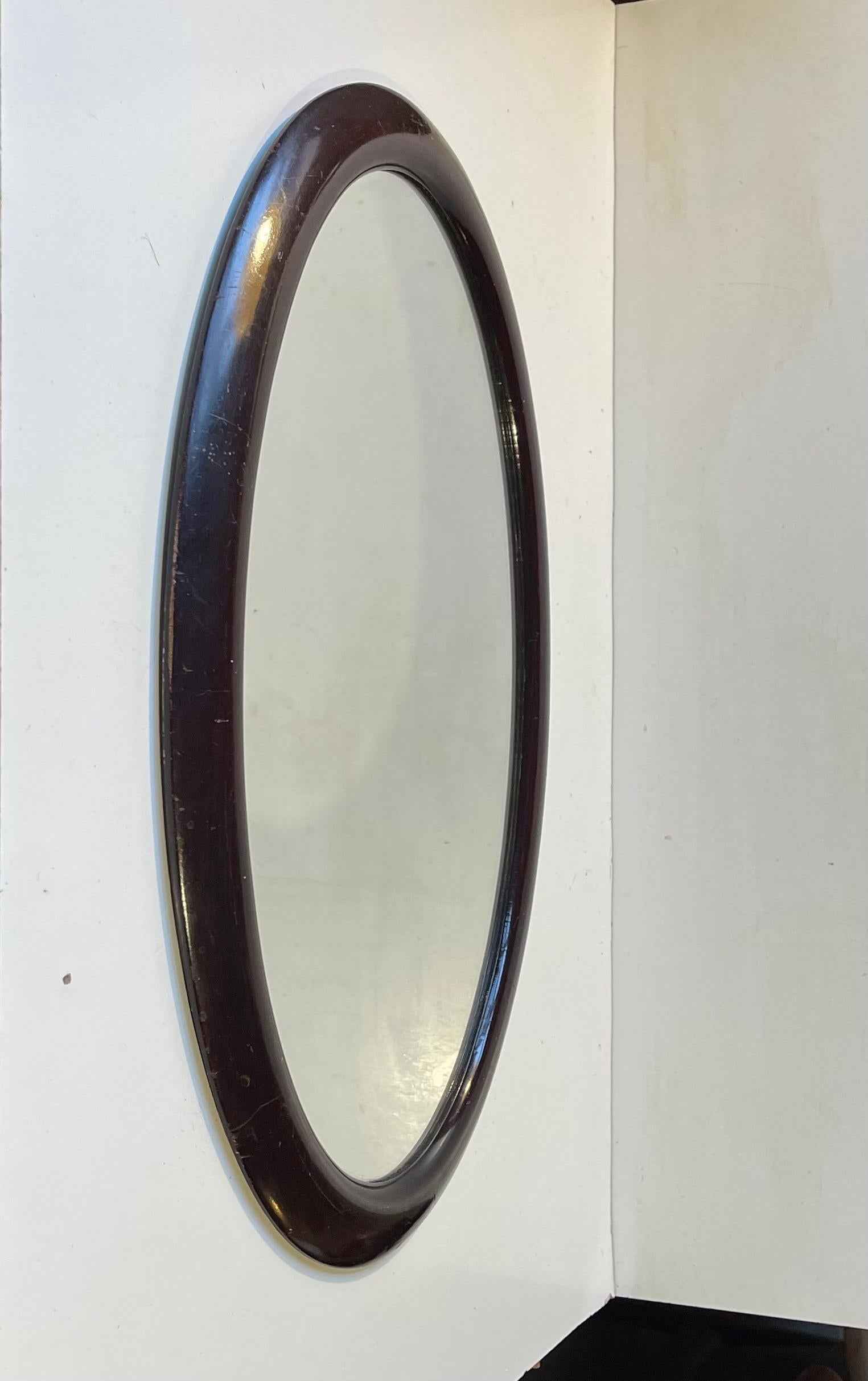A bend-wood wall mirror in stained oak (dark mahogany tone). Clean curves and simple lines in an oval shape. Made by a Danish cabinetmaker during the early 1920s. Measurements: 49x33x3 cm in framed.