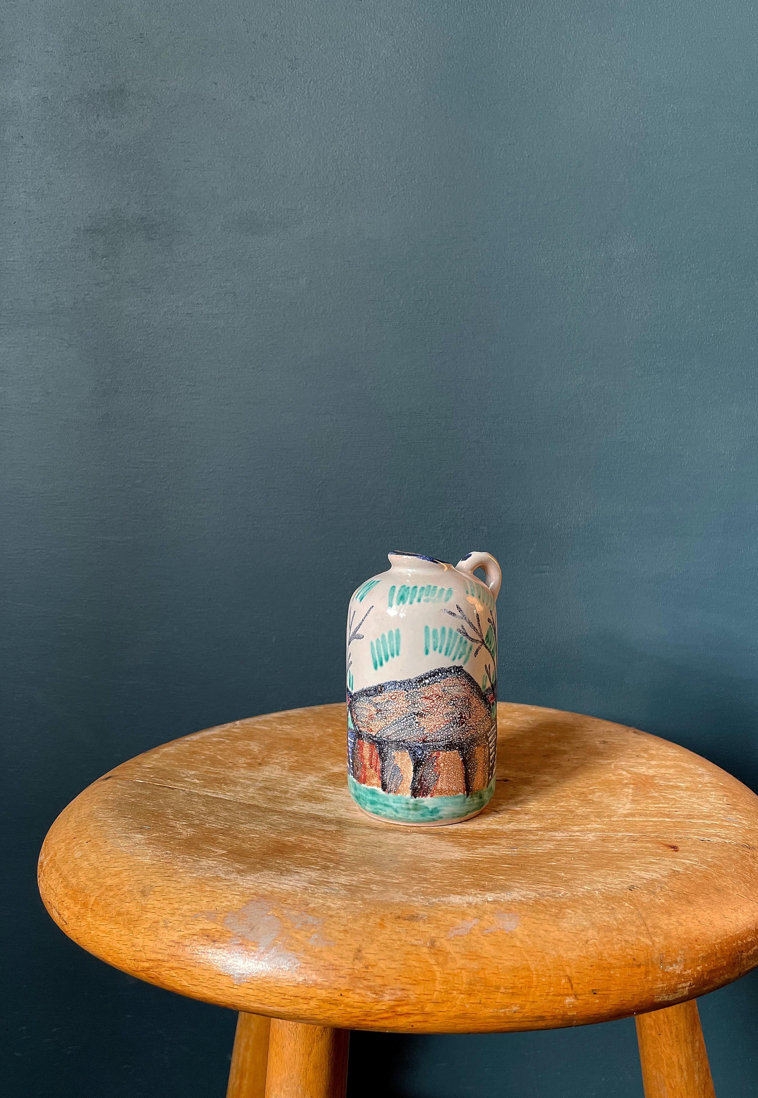 Small midcentury handpainted ceramic pitcher vase. Decorated with landscape motif of a Danish stone age viking grave built of large rocks. Multicolored unique decor on chalk white background. Blue glaze on spout, and small handle with blue dots.