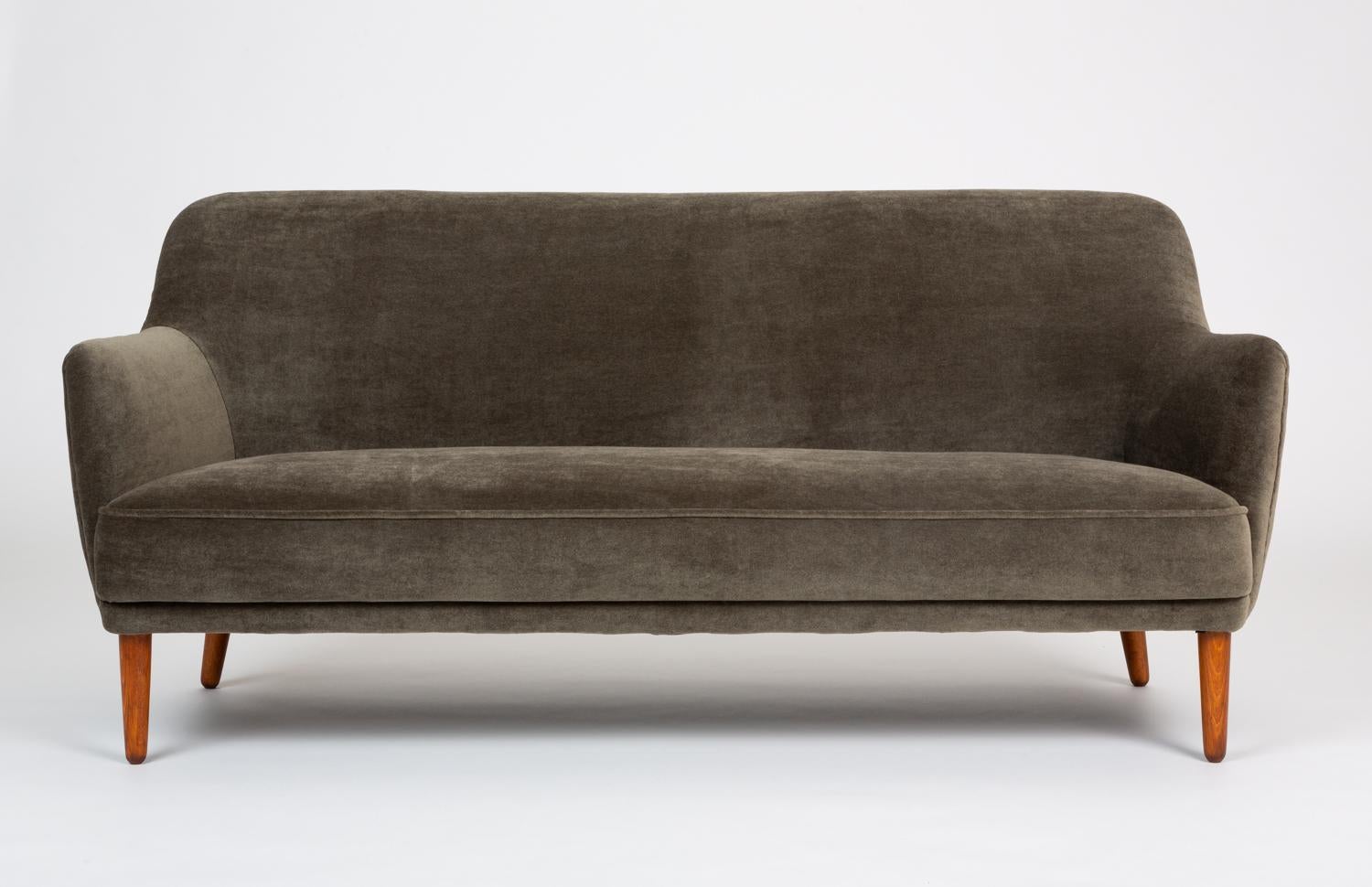 A Danish compact sofa with unbroken curves designed by John Vedel-Rieper and produced by Anker Petersen in the 1950s. The oyster-gray velvet upholstery is hand-stitched tight to the frame, emphasizing the design’s simple elegance. The seat is a