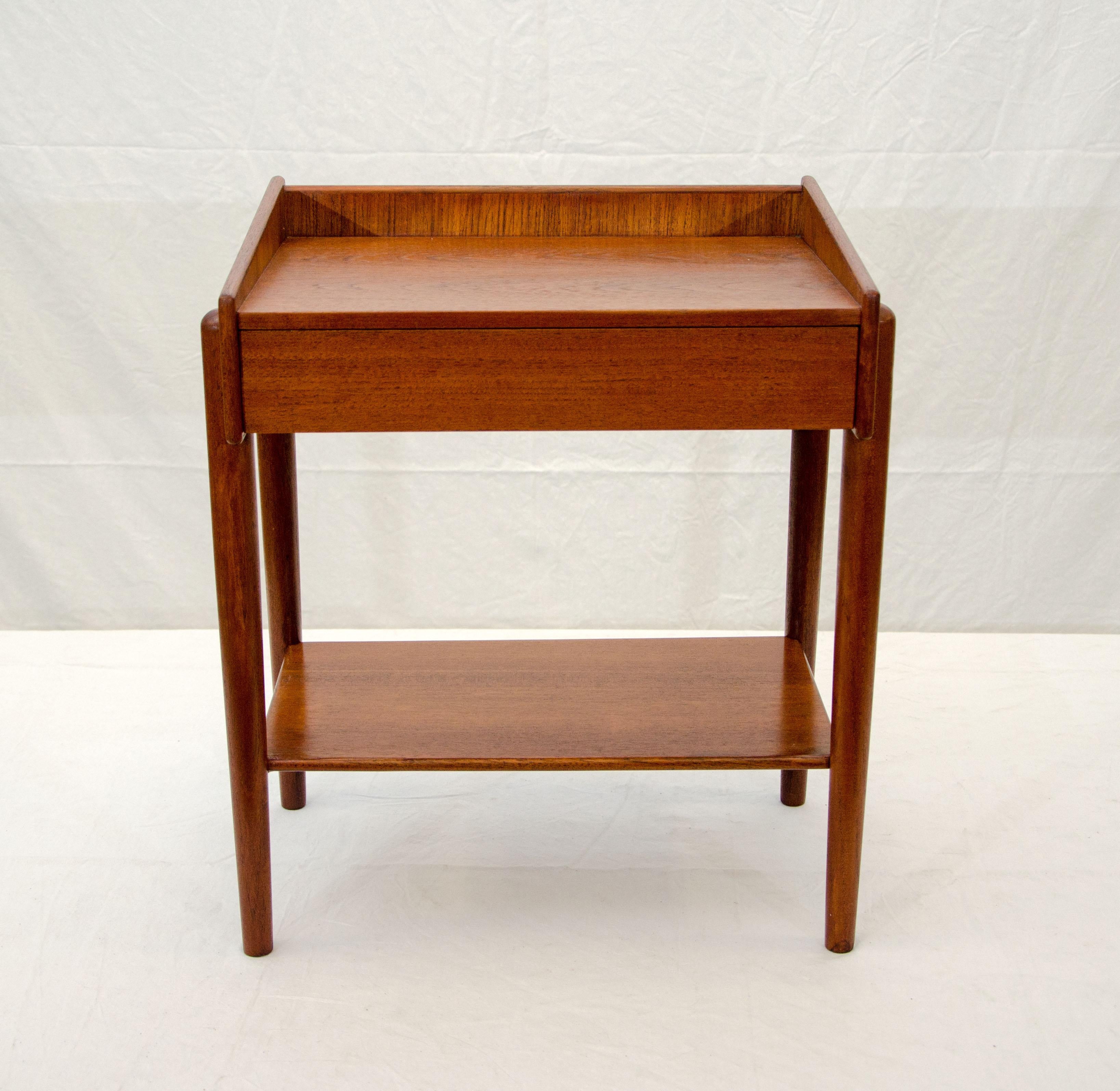 Nice small nightstand or end table with one storage drawer and a shelf on round tapered legs. The sides of the cabinet taper to a taller gallery at the back.