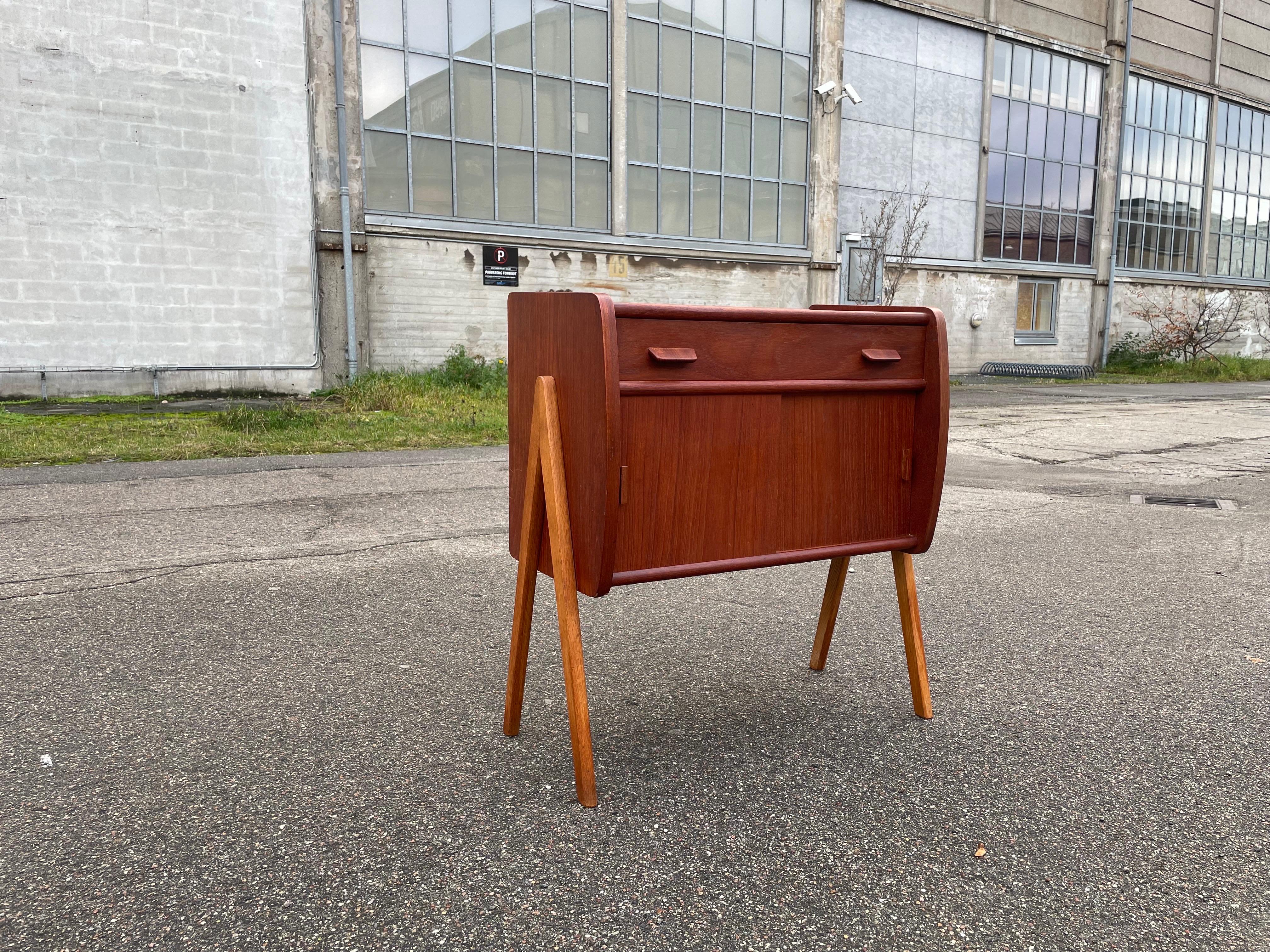 Gli am designs di Poul Volther incarnano l'estetica minimalista ed elegante del design danese, arricchita dal suo tocco distintivo. Un esempio è il suo mobile in teak, caratterizzato da gambe a forma di bussola che combinano l'intrigo visivo con