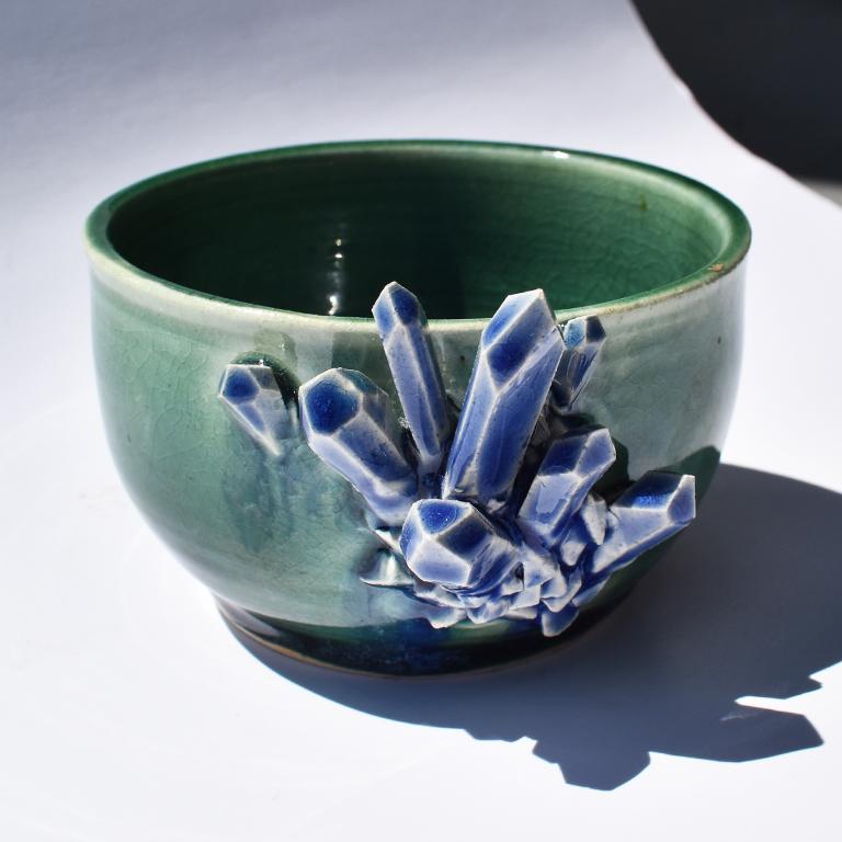 Ceramic bowl in green and blue with geode shaped detail at front. The exterior is a lovely green color, and blue glazed geode shaped ceramic pieces protrude at the front in blue. 

Inside the bowl at the bottom, a blue glaze has been applied,