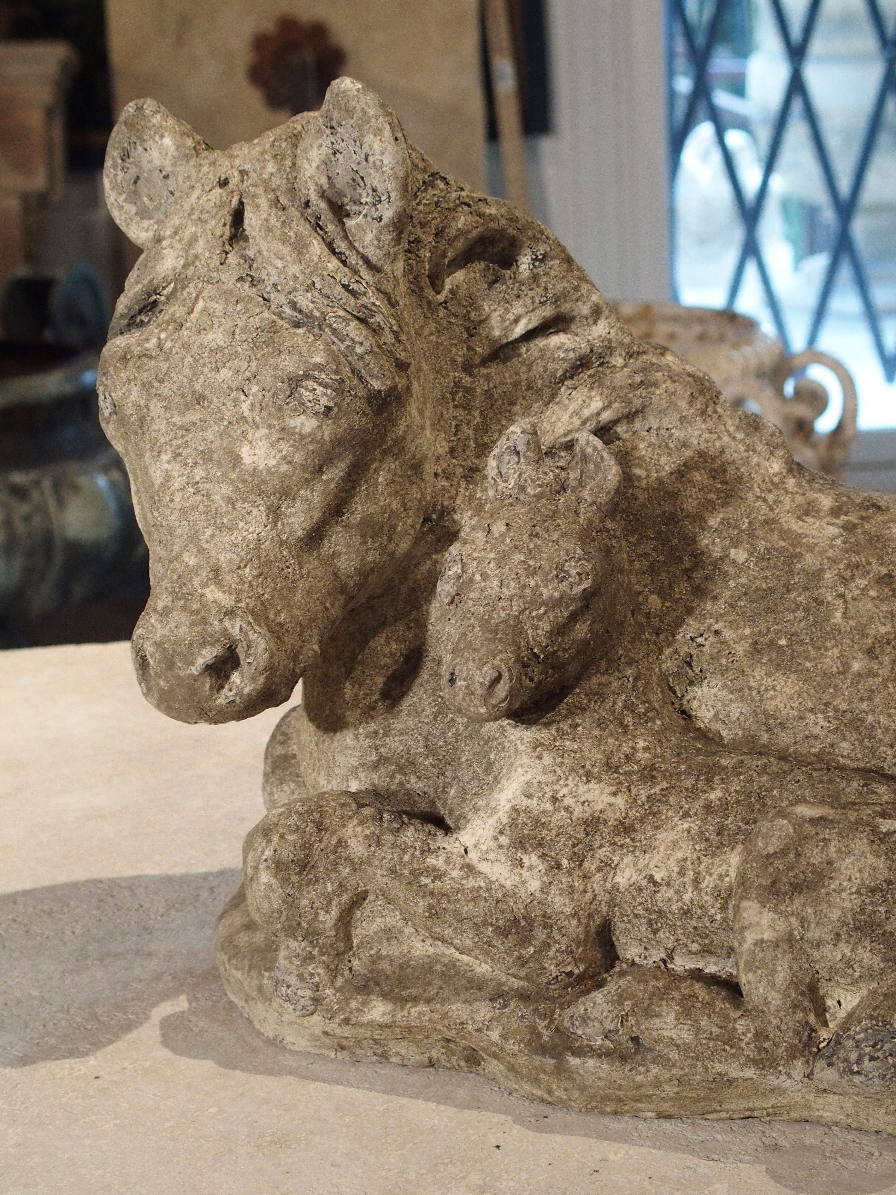 This unique little cast stone statue depicts two ponies curled up in a lying position. Both look forward attentively, with their front legs tucked beneath them. The statue has been outdoors for some time, and it has gained a nice natural patina that
