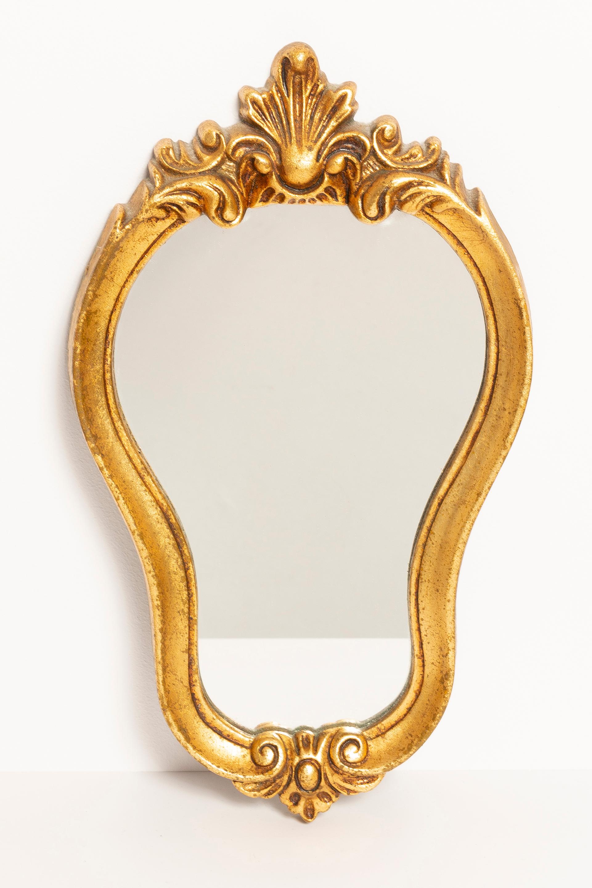 A beautiful small mirror in a golden decorative frame with flowers. Produced in 1960s in Europe/Italy. The frame is made of wood, painted in gold wood paint. Mirror is in very good vintage condition, no damage or cracks in the frame. Original glass.