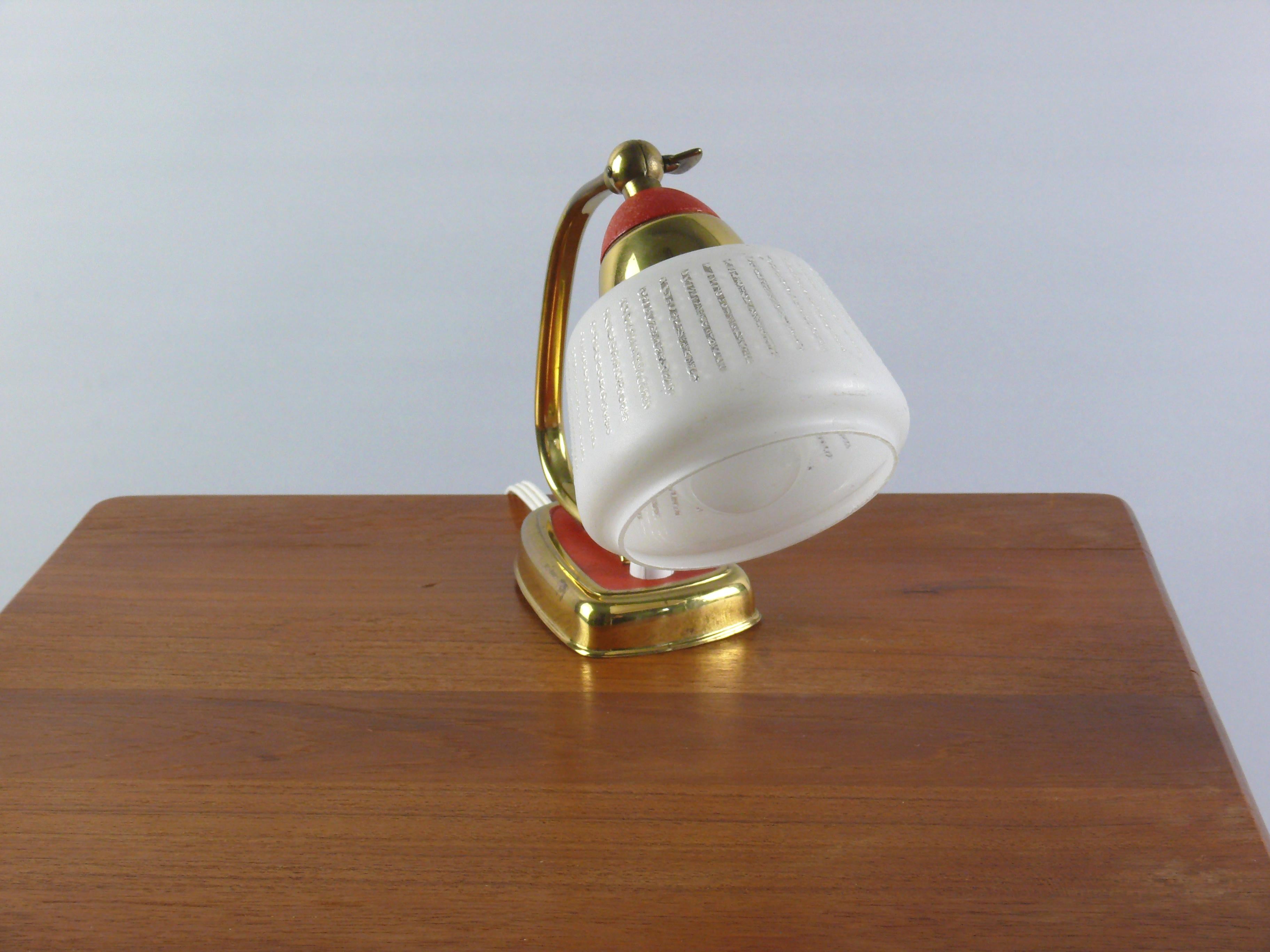 Lovely little table lamp from the 1960s. Textured opal glass shade with shrink varnish glass holder and base, brass arm and brass base surround. Rounded, trapezoidal brass base with pressure switch. The shade can be adjusted via a joint with a