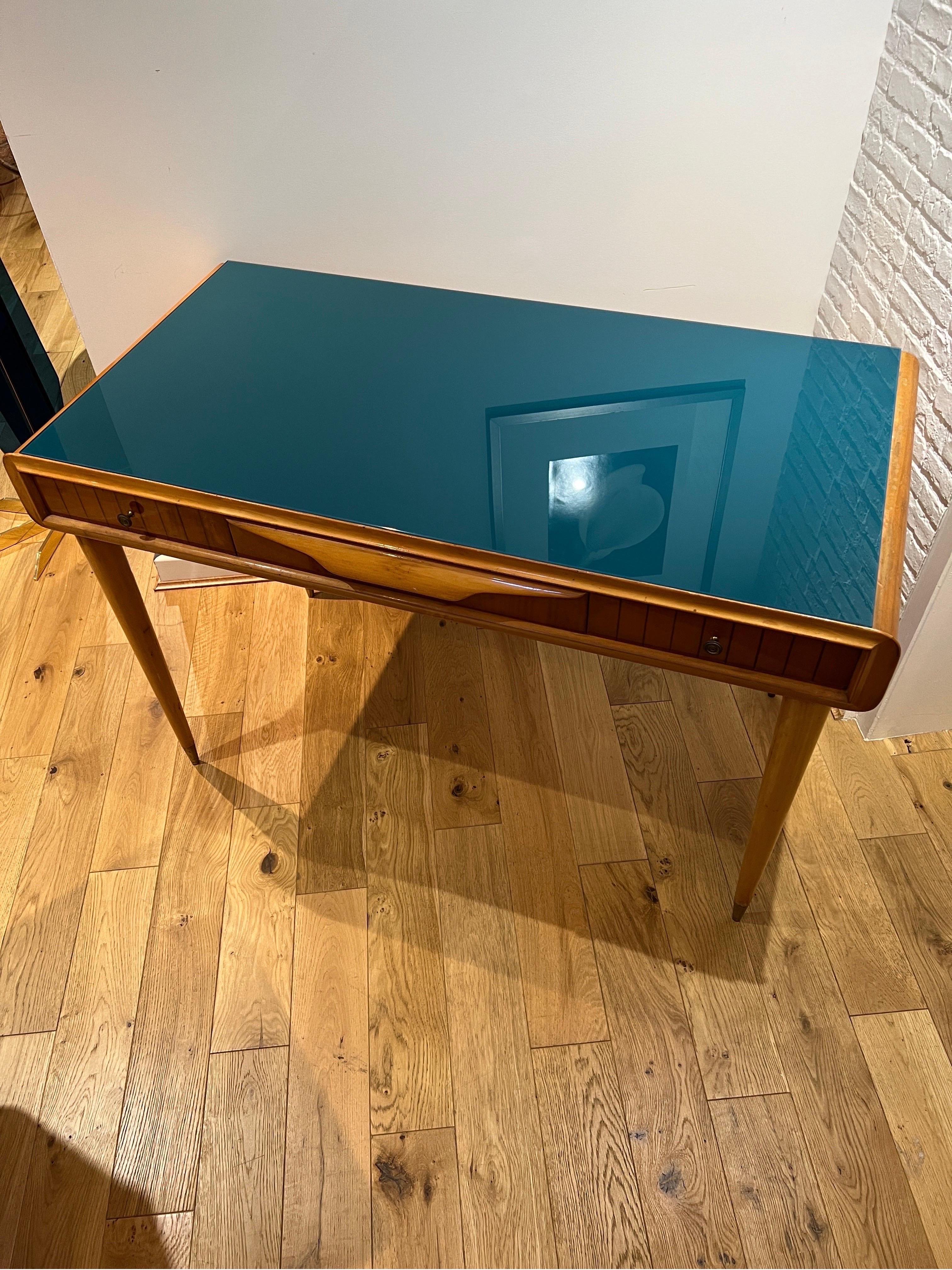 A 1950s Italian 3 drawers desk in cherrywood with laminated stripe detailing on the front and a beautiful blue glass on top . Brass handles and brass sabots on the legs . This elegant & versatile piece can also be used as a console or a vanity table