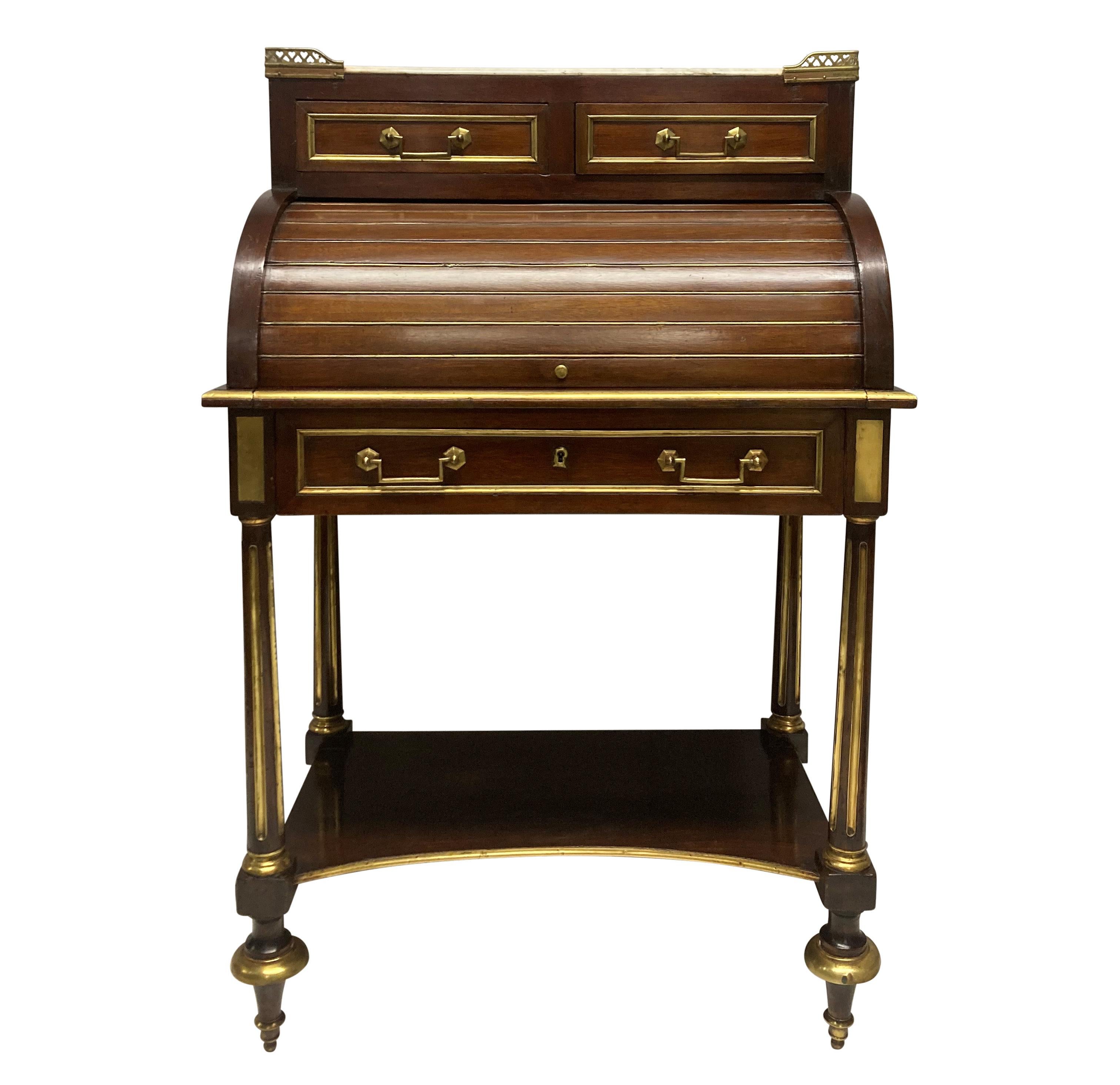 A small French Directoire mahogany cylinder desk, with brass detailing throughout. The roll top hiding a witing slope with a tooled leather top and two drawers. Above, a marble galleried top with two drawers below. The gallery pierced with hearts.