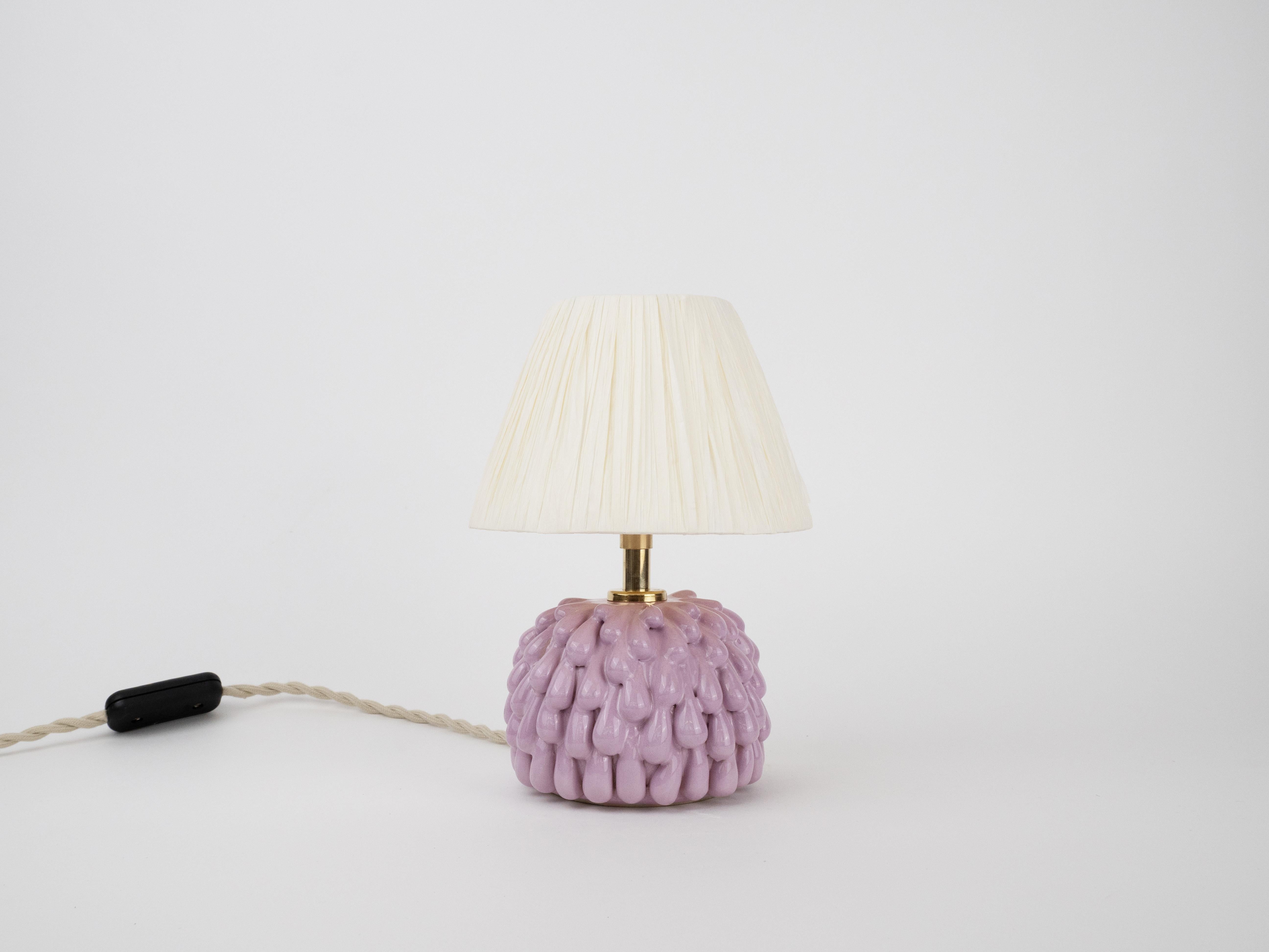 Meet your new tiny beacon of coziness. This adorable handmade ceramic lamp has a glossy violet base with a playful drippy texture. Topped with a delicate paper raffia shade, it casts a soft, warm glow - perfect for dreamy evenings.

Bulb is