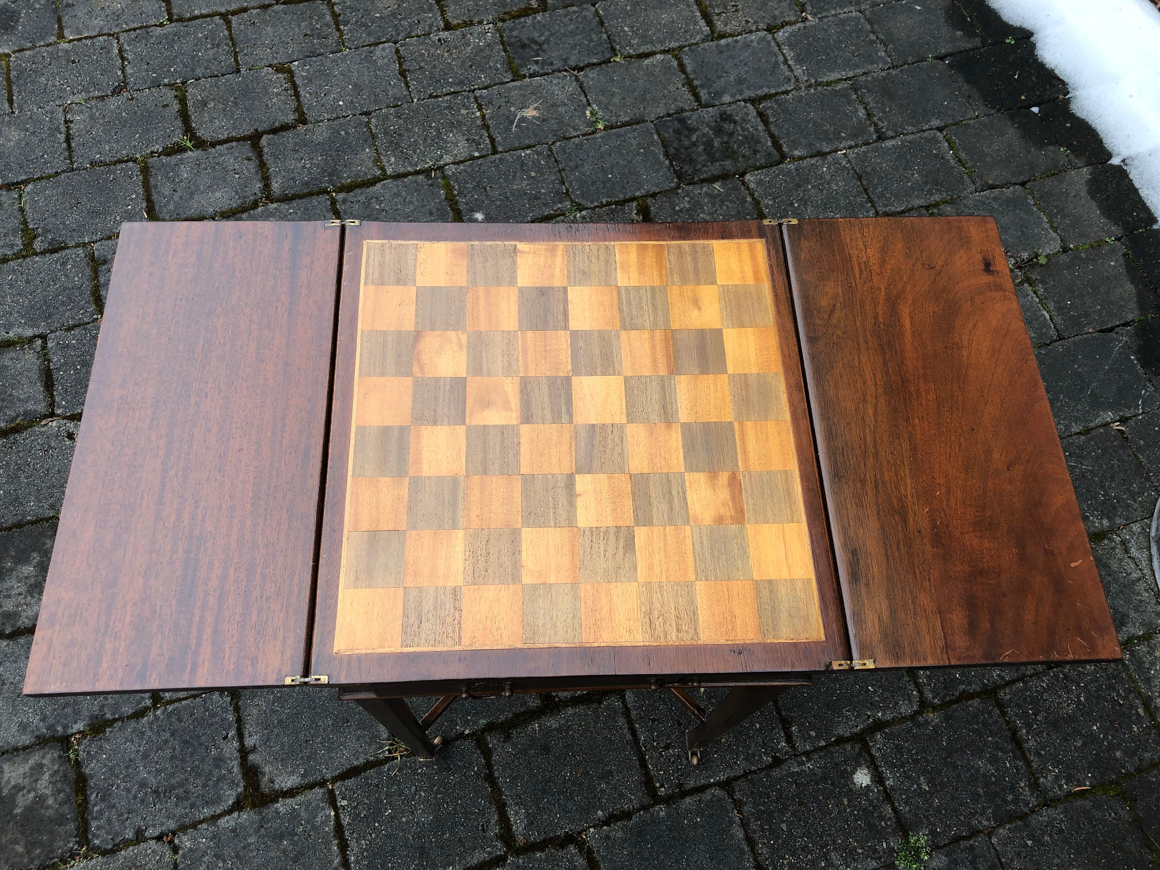 A small game table with inlaid board.

The sides pull out to form supports for the top.

Brass caster feet.
 