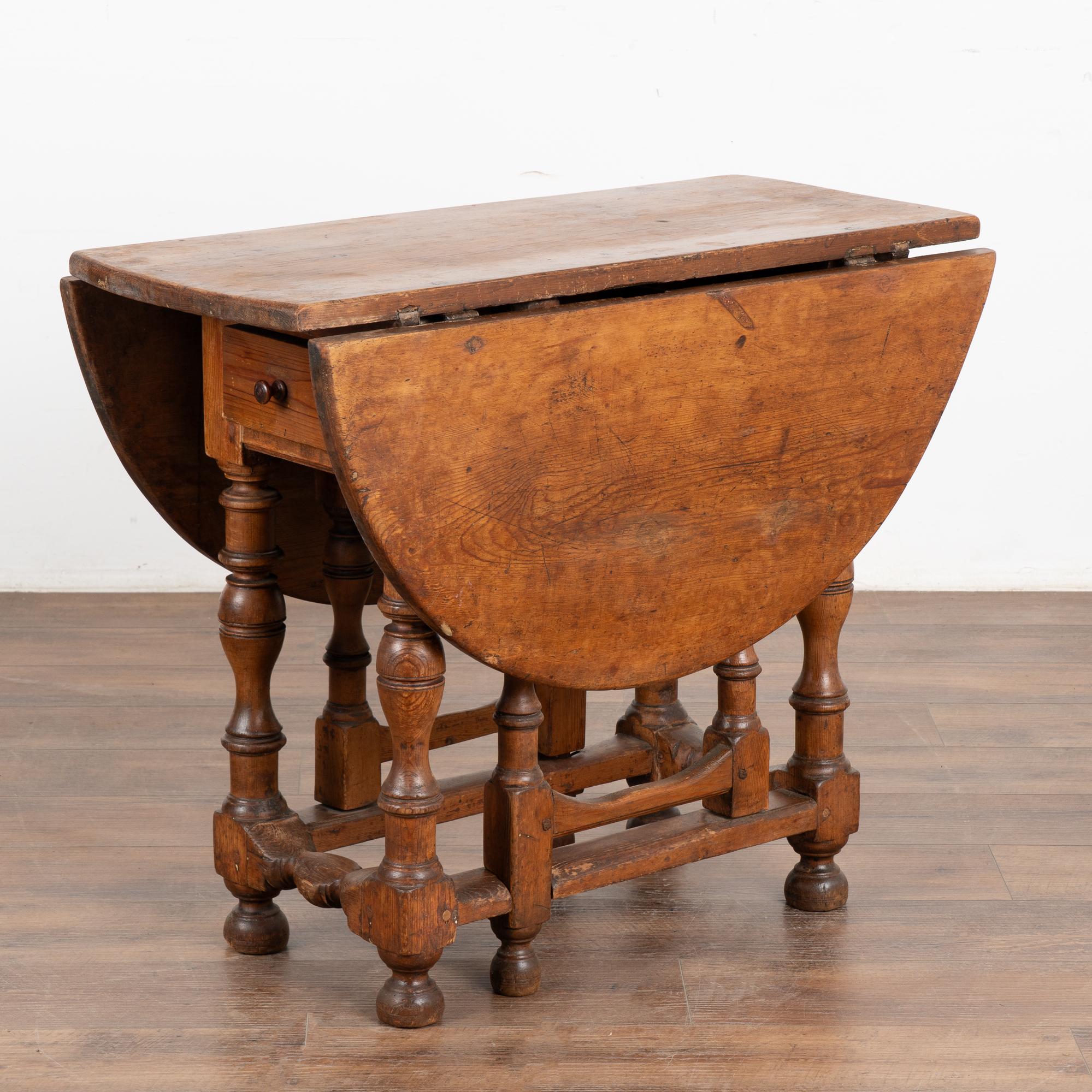 There is wonderful aged charisma to this drop leaf gate leg table that can serve as a side table, small console or even kitchen table.
Unique to this table is the single long drawer and lovely turned legs. The pine has a very deep, rich patina due