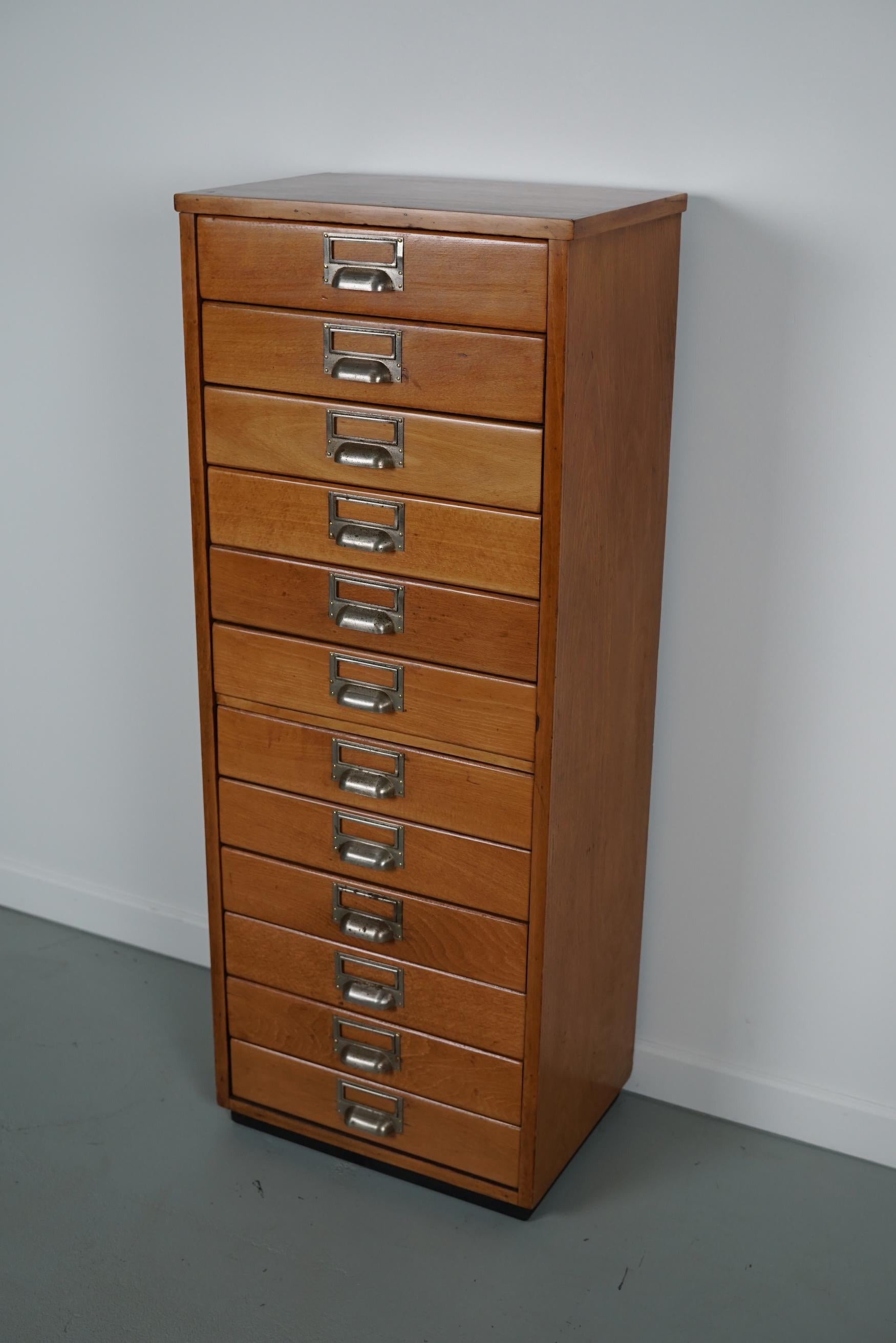 This Dutch apothecary cabinet was made circa 1950s in the Netherlands. It features 12 drawers with metal cup handles. It is made from beech wood. The interior dimensions of the drawers are D x W x H: 22 x 33 x 6 cm.