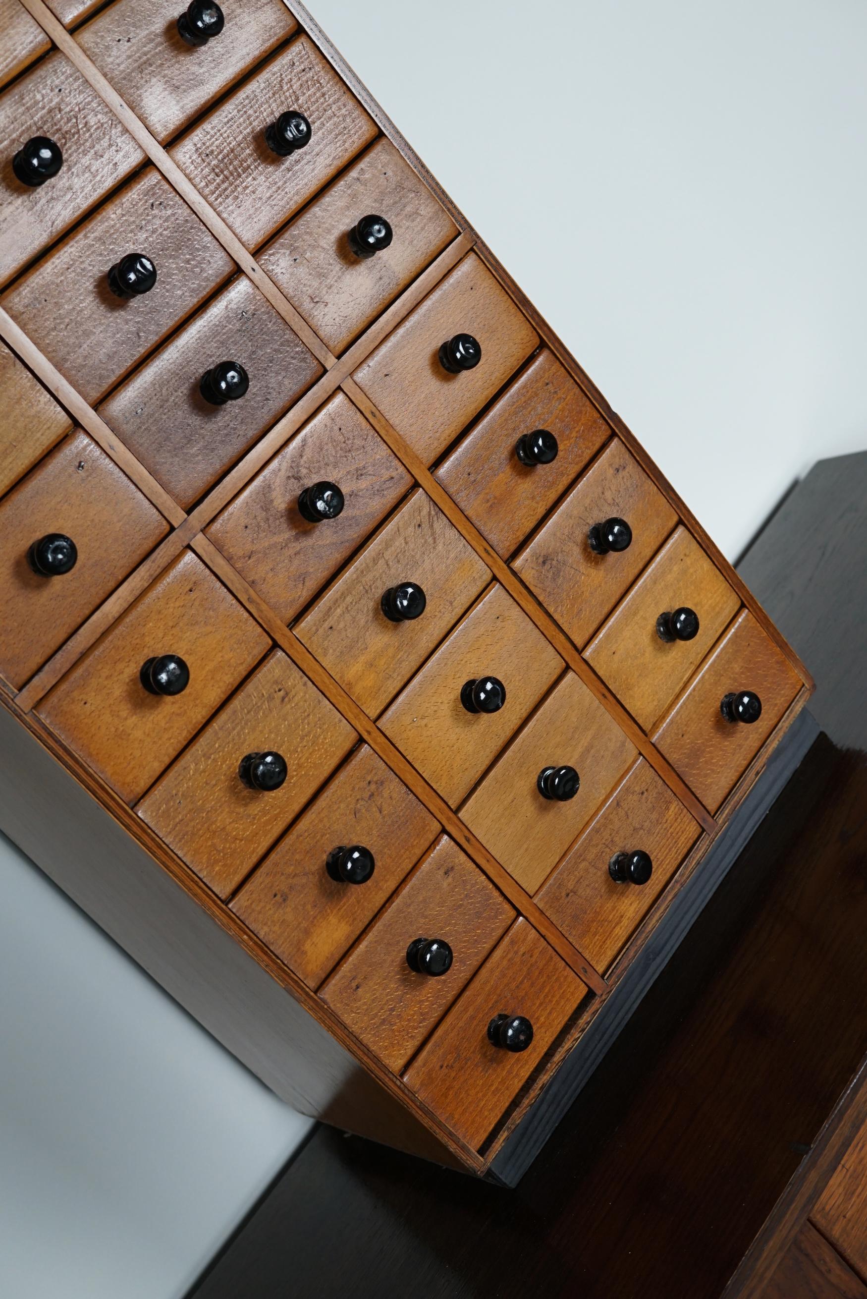 This tabletop cabinet was made around the 1950s in the Netherlands. It features 27 small drawers with black metal knobs. It remains in a good condition. The interior dimensions of the drawers are: D 18 x W 10 x H 5 cm.