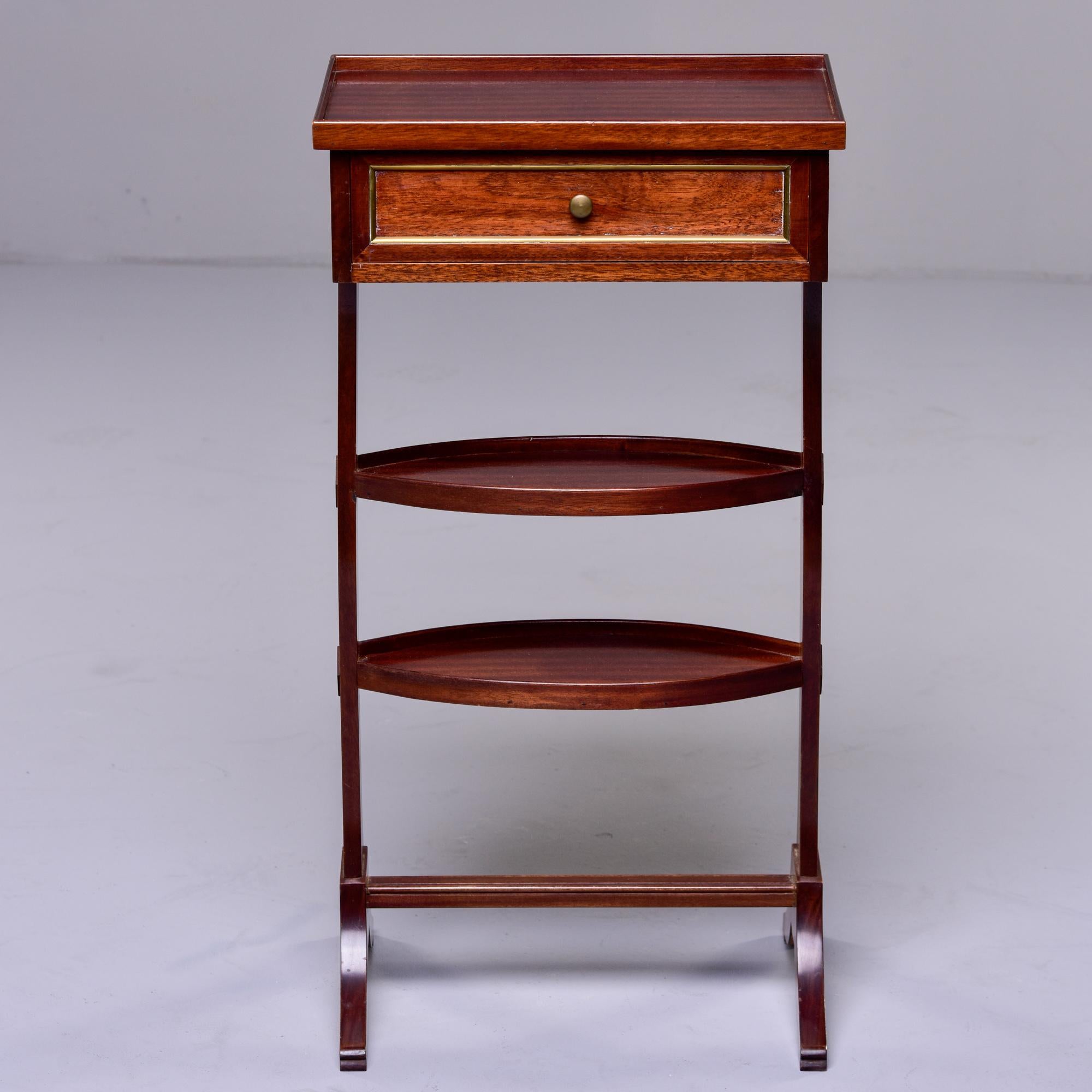 Circa 1930s small mahogany French side table with footed base, two small oval shelves and rectangular top with single brass-trimmed drawer. Unknown maker.