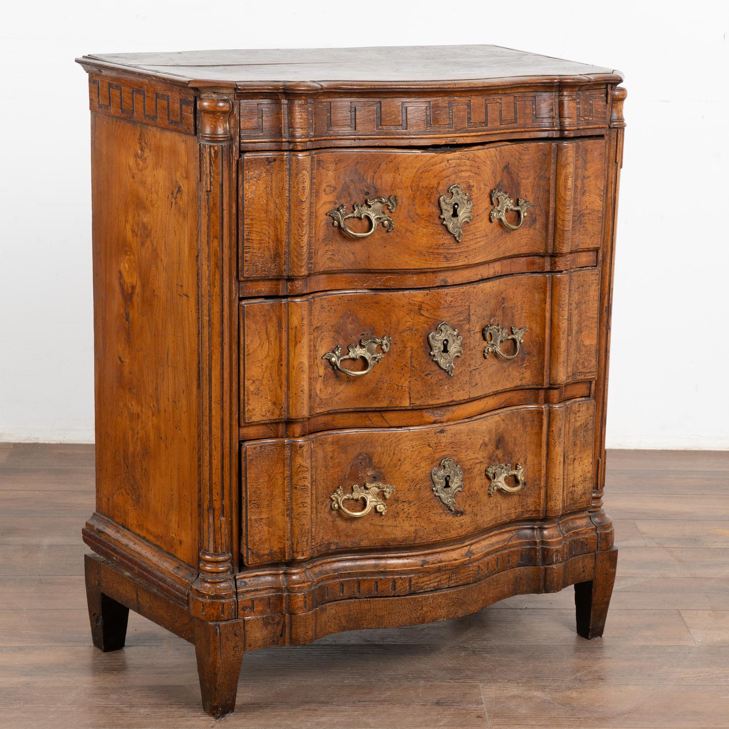 A Danish late 18th century Louis XVI chest of three drawers. Serpentine front topped with carved Greek key motif.
The dark, rich patina of the elm wood reflects generations of use. Note cracks/separation of wood in particularly the top and