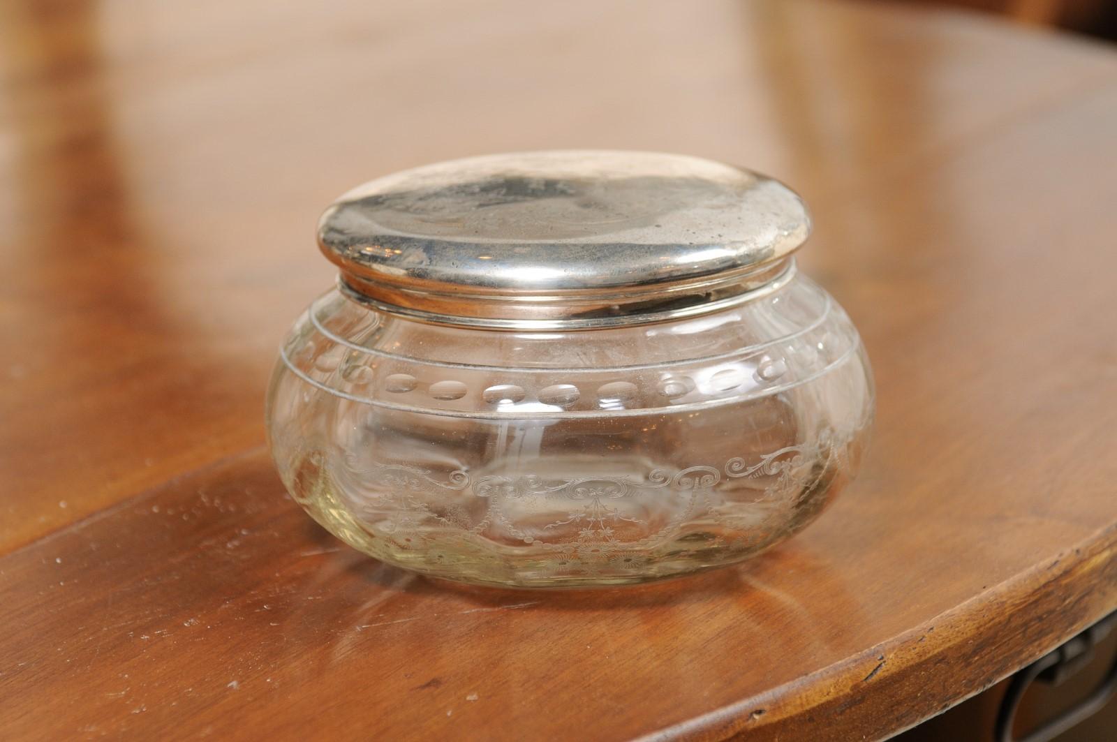 A small English glass vanity jar from the early years of the 20th century, with incised silver lid and etched design. Created in England during the first quarter of the 20th century, this petite jar features a circular glass body adorned with a