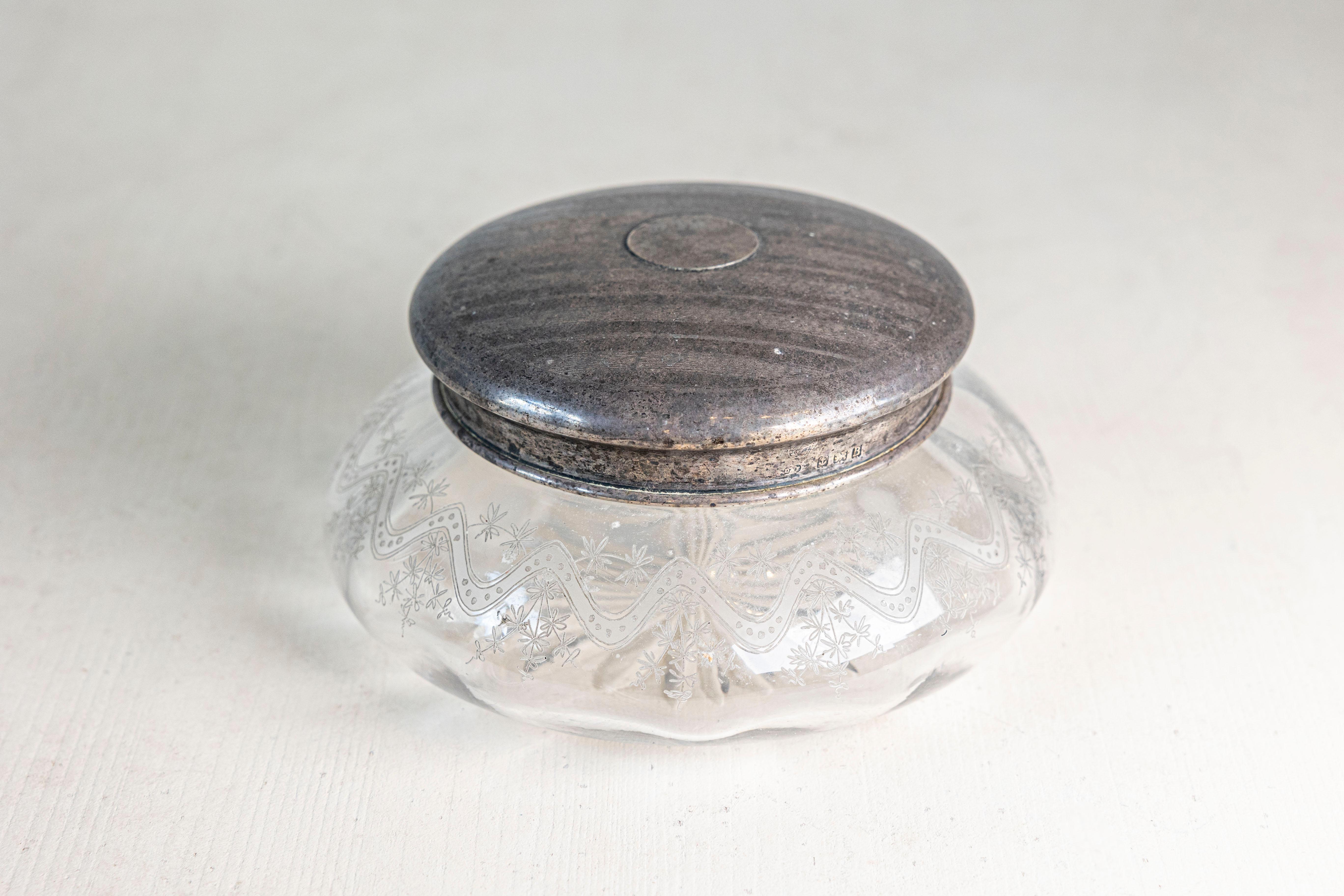 Piccolo vaso da notte in vetro inglese dei primi anni del XX secolo, con coperchio in argento inciso e disegno inciso. Creato in Inghilterra nel primo quarto del XX secolo, questo piccolo vaso presenta un corpo circolare in vetro ornato da un