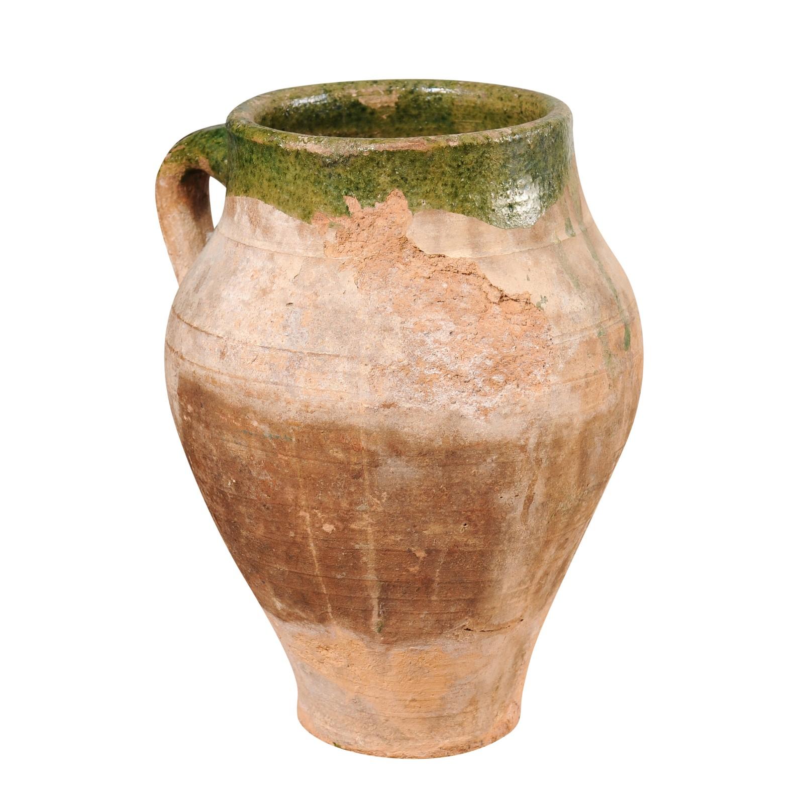 A small English terracotta olive oil jar from circa 1930 with green glaze and back handle. This small English terracotta olive oil jar, dating back to around 1930, exudes rustic charm and vintage character. Its unassuming yet captivating appearance