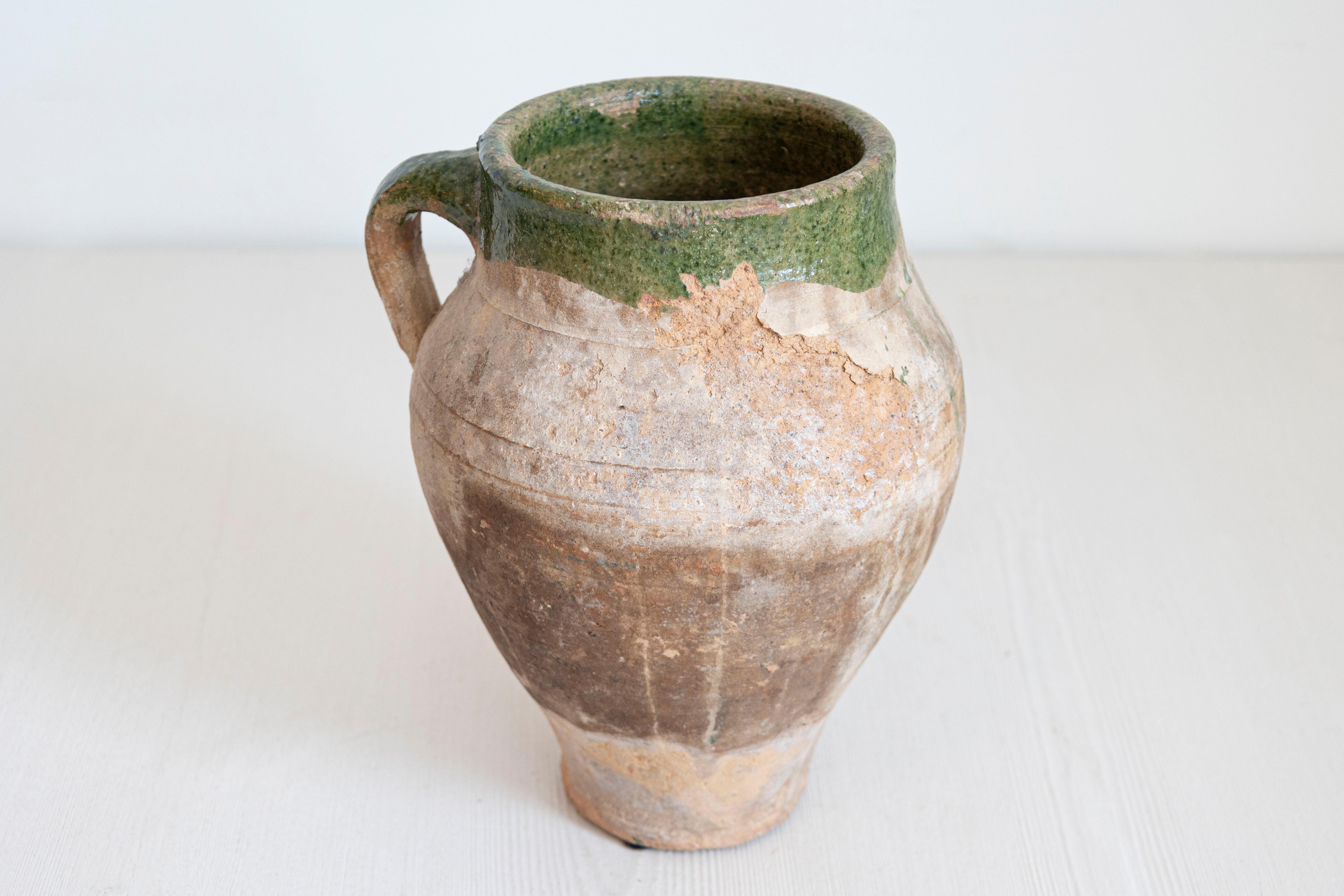 Un piccolo vaso da olio in terracotta inglese del 1930 circa con smalto verde e manico posteriore. Questo piccolo orcio di terracotta inglese, risalente al 1930 circa, emana un fascino rustico e un carattere vintage. Il suo aspetto discreto ma
