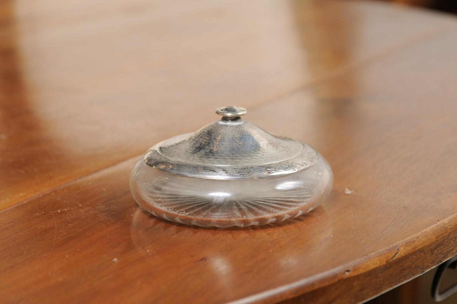 A small English Victorian period glass vanity jar from the 19th century, with silver lid and etched design. Created in England during the 19th century, this petite bottle features a circular glass body adorned with delicately etched radiating motifs