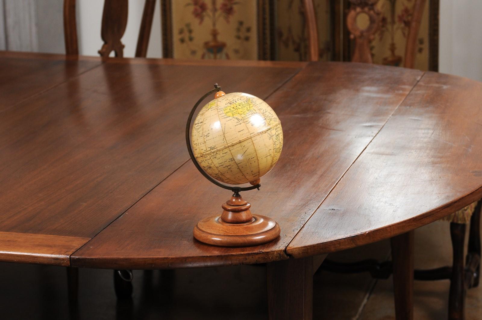 A small English terrestrial globe from the 20th century, with brass protractor and circular wooden base. Created in England during the 20th century by George Philip & Son in London, this terrestrial globe is connected through a brass protractor to a