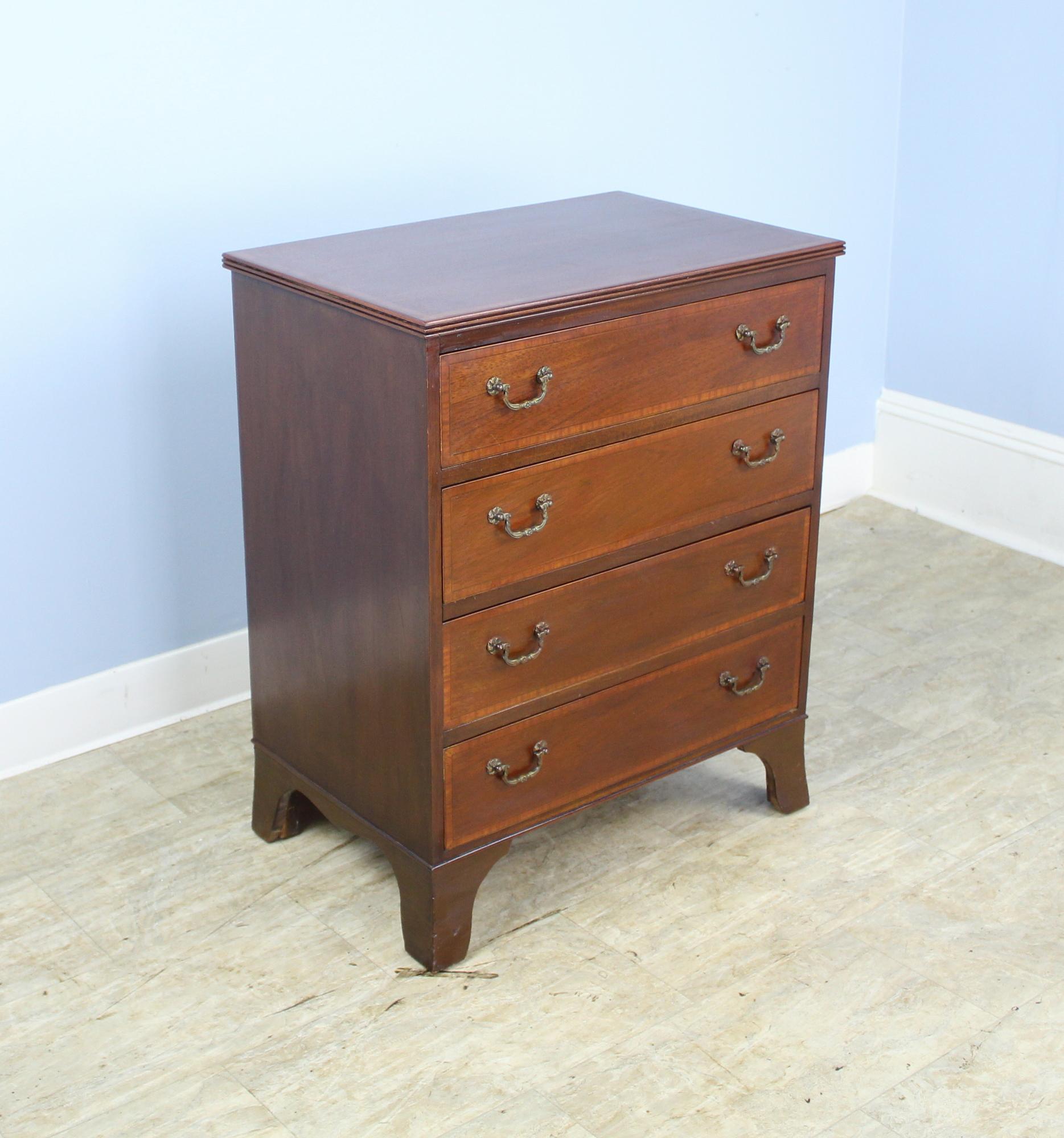 A diminutive chest of drawers with a grand personality! Rich mahogany with kingwood banding around the drawers and top. Small reeded detail along the edge of the top.  Stylized flared feet and sweet drop handles. This would work well in a child's
