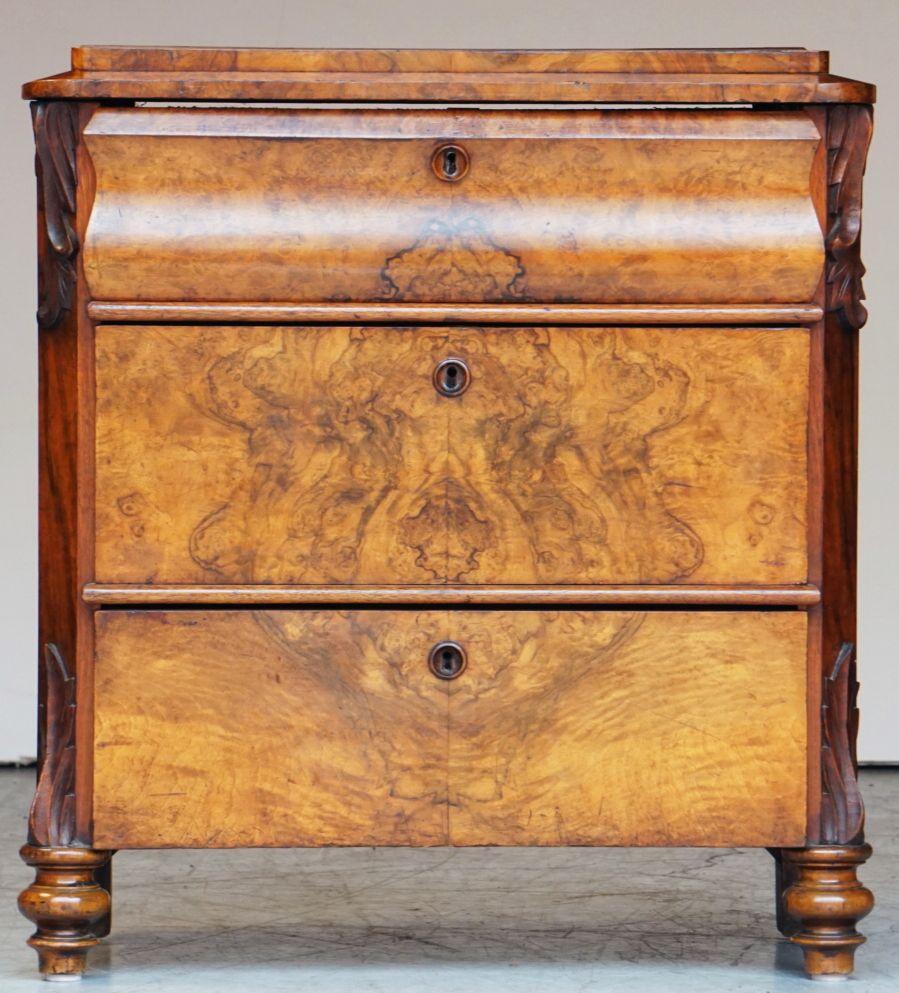 A fine English small chest of drawers or commode of patinated burr walnut, featuring a moulded top over a frieze of three drawers, canted corners with a decorative relief of acanthus leaves at top and base, the top drawer with shaped facade, each