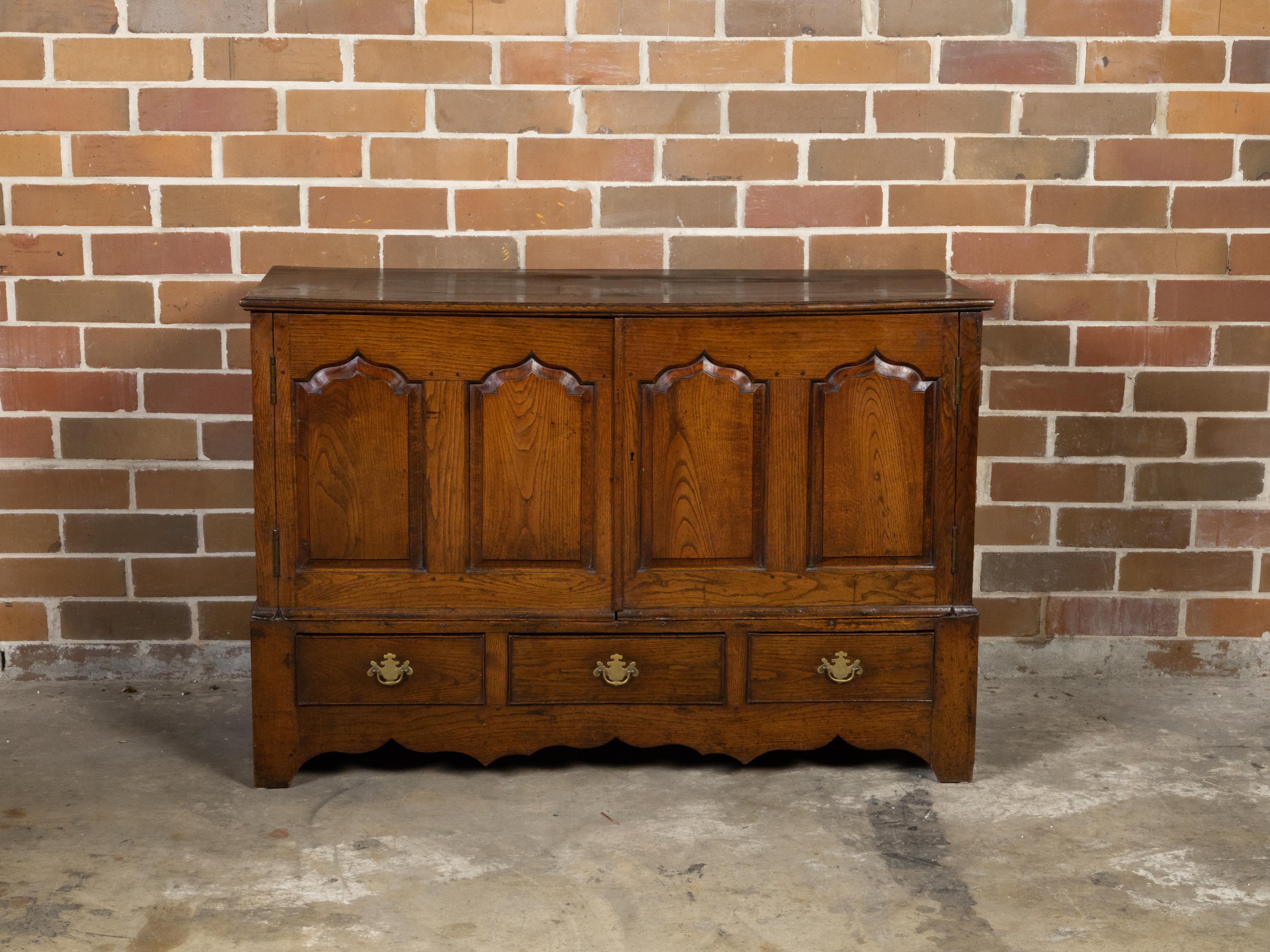 An English Georgian period small oak buffet from the 18th century, with double doors, drawers, arching motifs and brass Chippendale style hardware. Created in England during the Georgian era in the 18th century, this small oak buffet features a