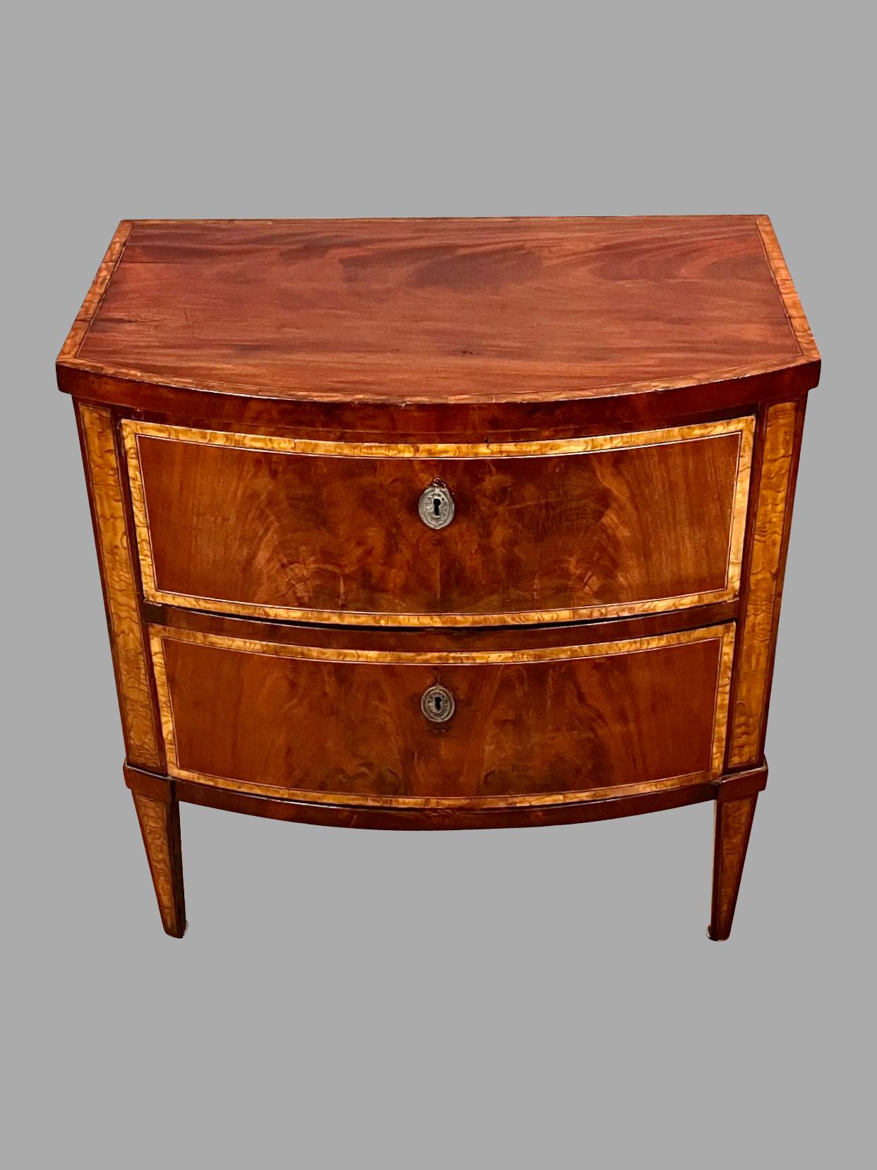 A handsome English Hepplewhite inlaid mahogany 2 drawer bow front commode of desirable small size, the overhanging top crossbanded in burl elm over 2 similarly inlaid drawers all supported on square tapered legs. This is a useful and versatile piece