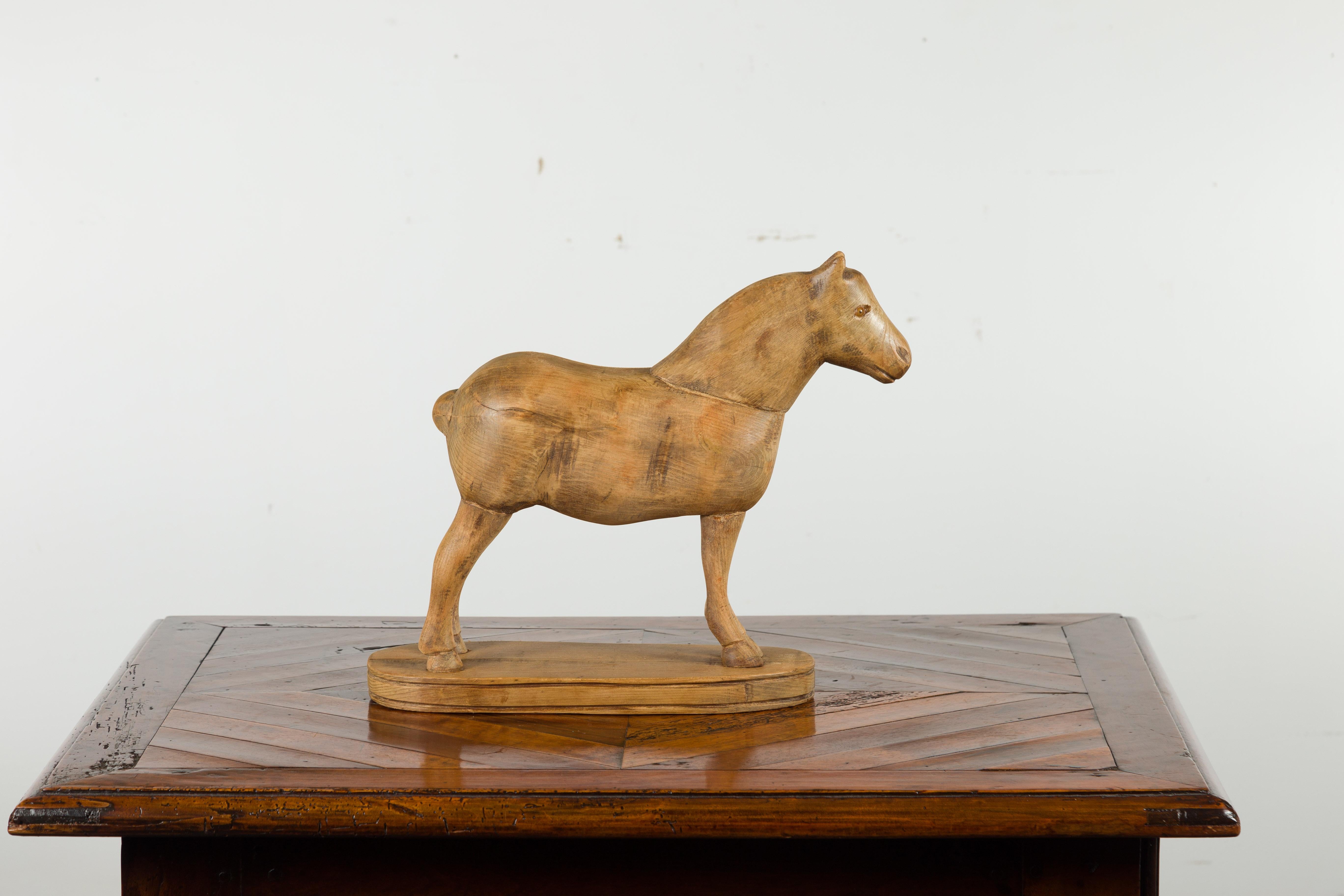 A small English carved pine horse from the early 20th century on oval base. Carved in England during the early years of the 20th century, this small pine horse charms us with its petite proportions and archaic style. Standing proudly on an oval