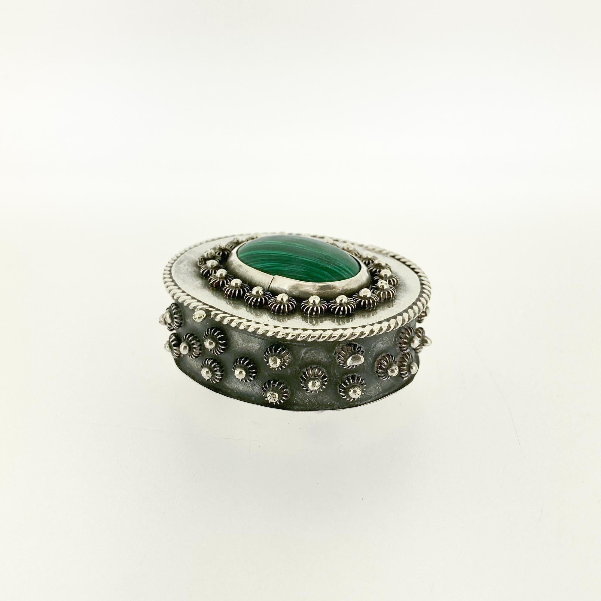 A fine Mexican sterling silver box.

With a malachite cabochon to the lid surrounded by silver knops. 

The rim of the lid is braided, and the side of the body is decorated with knops throughout.

The box stands on 4 small knop shaped feet.

Marked
