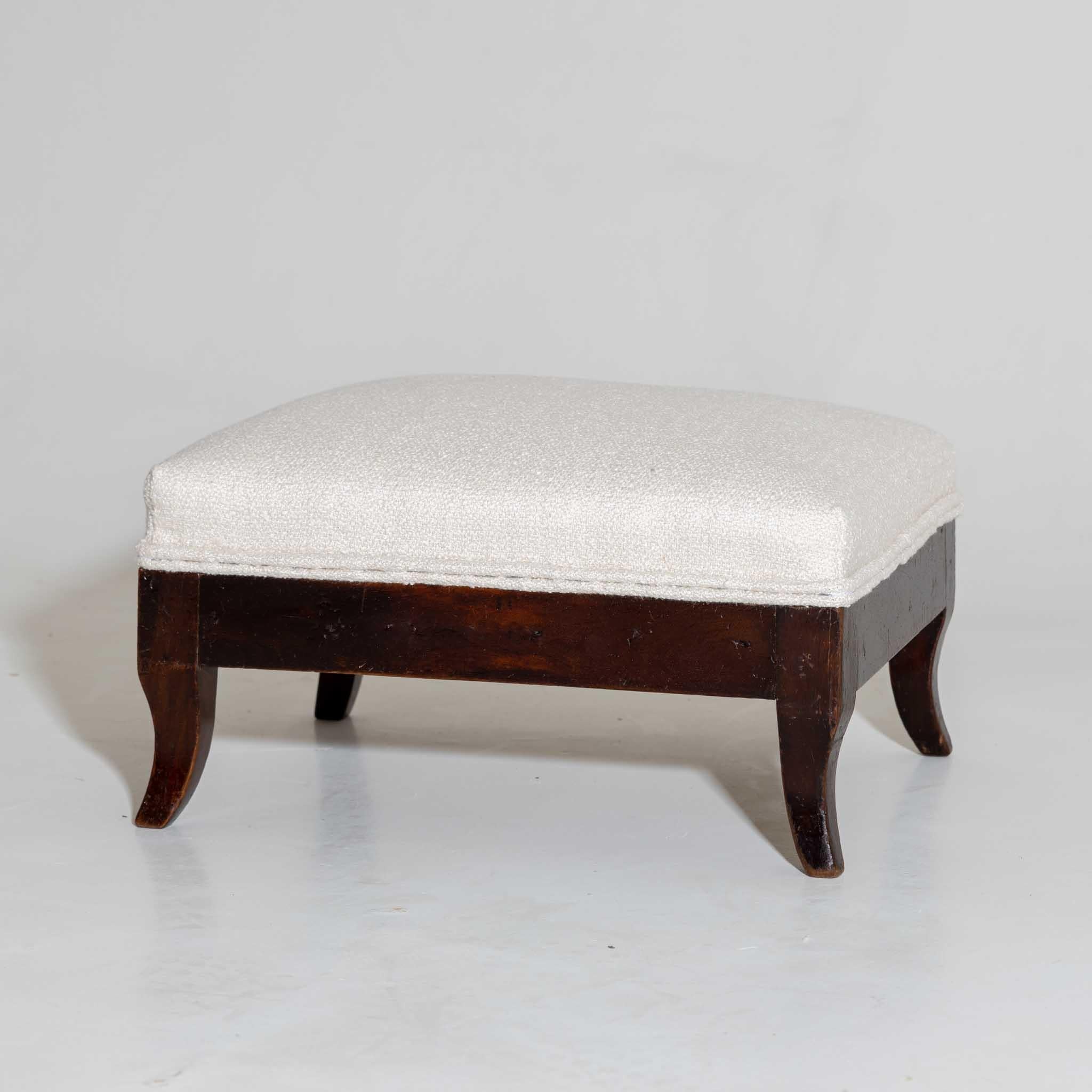 Small footstool on small sabre legs with straight frame in walnut and upholstered top. The footstool was covered with a white bouclé fabric.