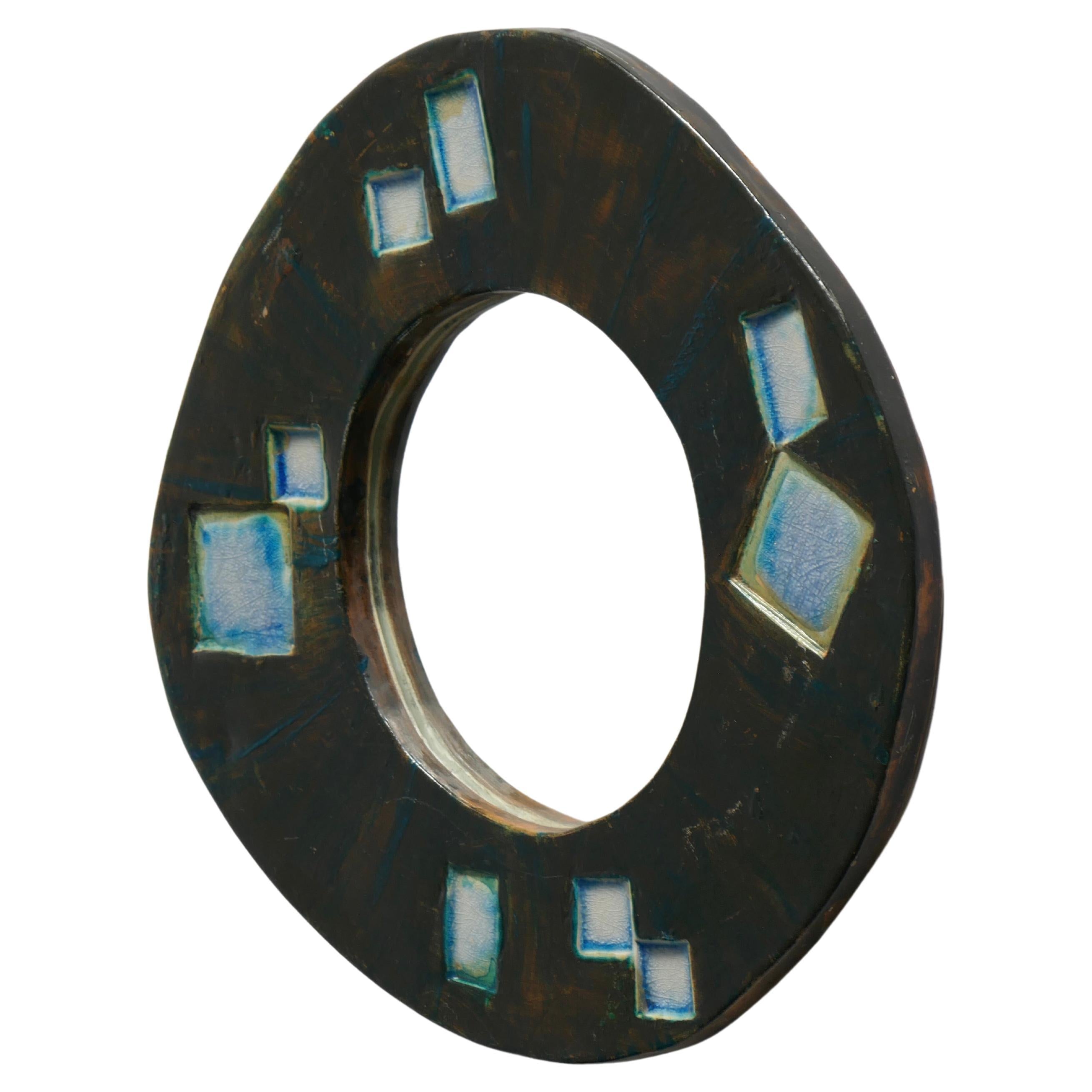 Small free shape ceramic mirror in black and brown shades, embellished with blue and creamy white geometric patterns. French work from the 1960s. This very decorative mirror can be presented as a wall mirror. It does not have a hook on the back but