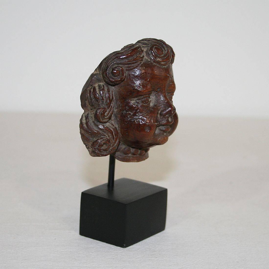 Very small Baroque carved wooden angel face, Frankrijk, circa 1650-1750. 
Weathered. Measurement with the base.