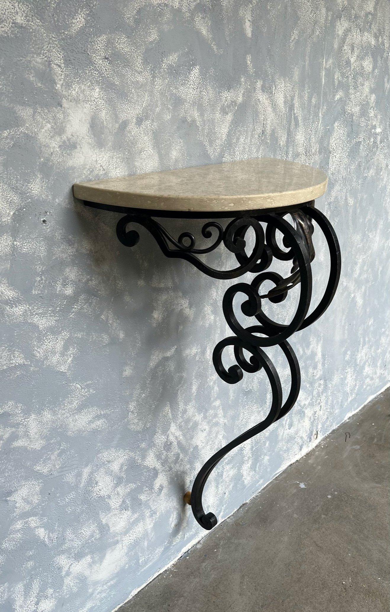 This small demilune wrought iron console is French from the 1940s or 1950s. The heavily scrolled black wrought iron base supports a beautiful travertine top. The console attaches to the wall in 2 places and is made to rest against the wall at a
