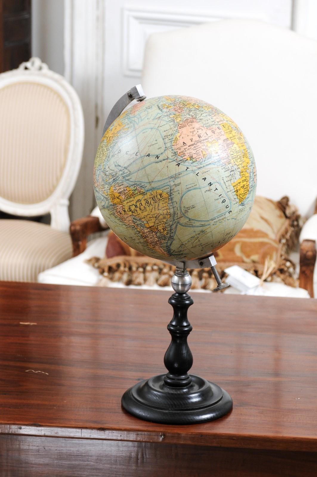 A small French terrestrial globe from the 20th century, with metal protractor and circular black wooden base. Created in France during the 20th century, this terrestrial globe is connected through a metal protractor to an elegant circular turned