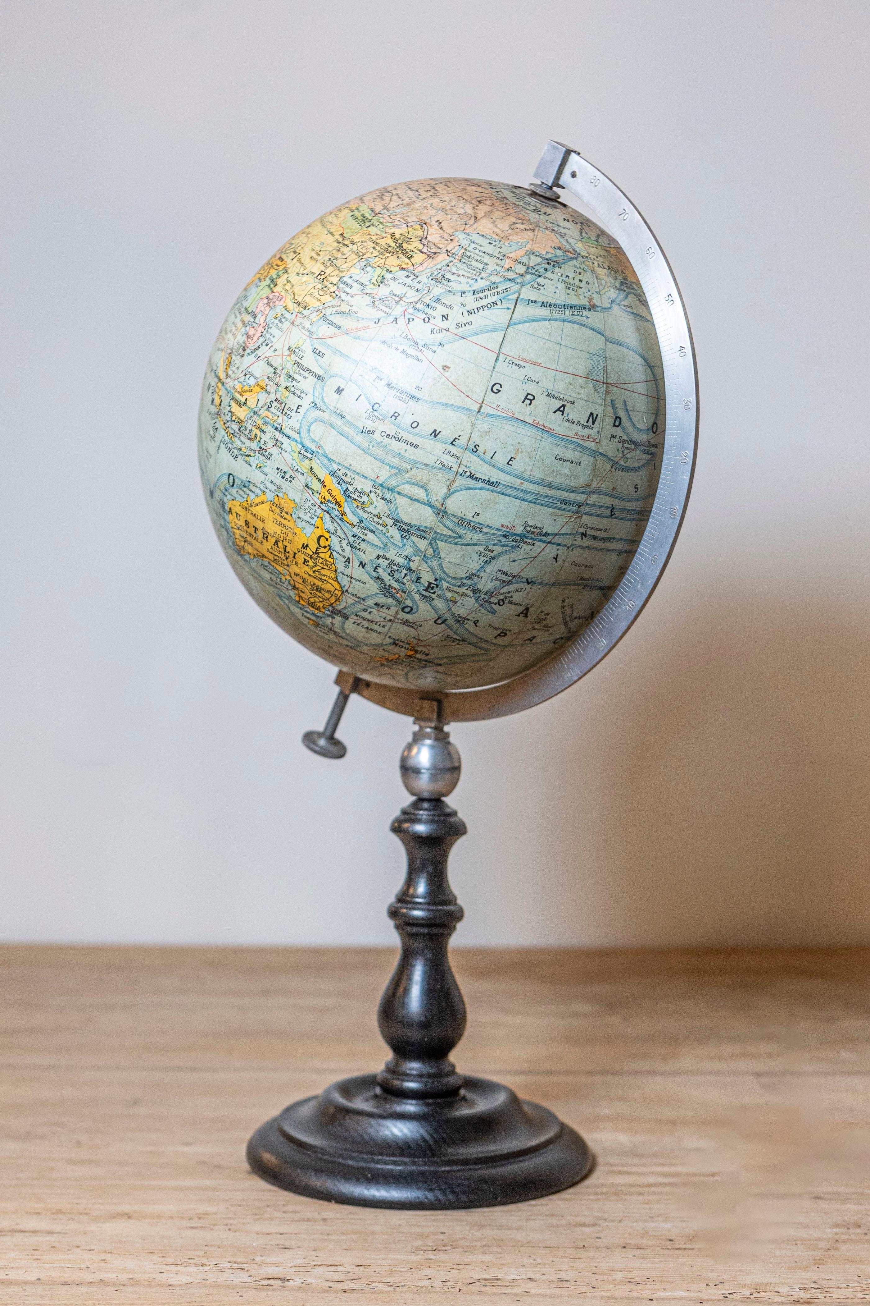 Petit globe terrestre français du 20e siècle, avec rapporteur en métal et base circulaire en bois noir. Créé en France au cours du XXe siècle, ce globe terrestre est relié par un rapporteur en métal à une élégante base circulaire en bois tourné